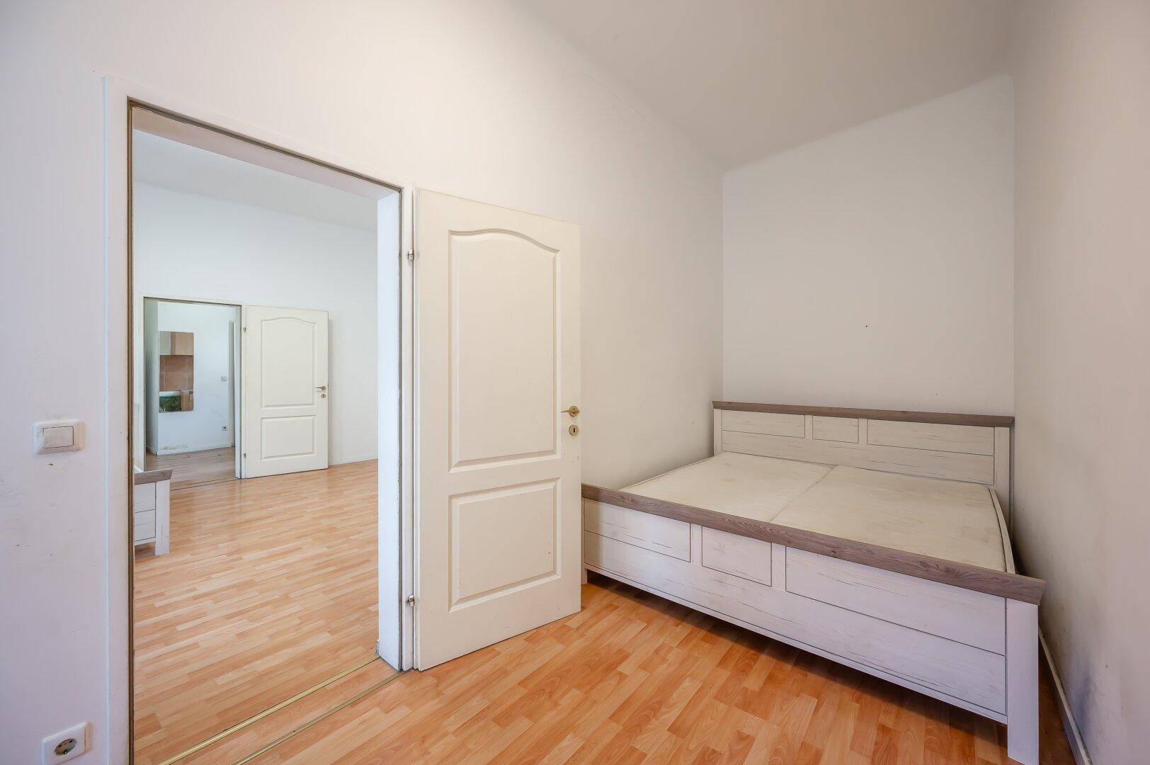 Schlafzimmer mit Holzboden und einem Bettgestell, das zu einem weiteren Raum führt.