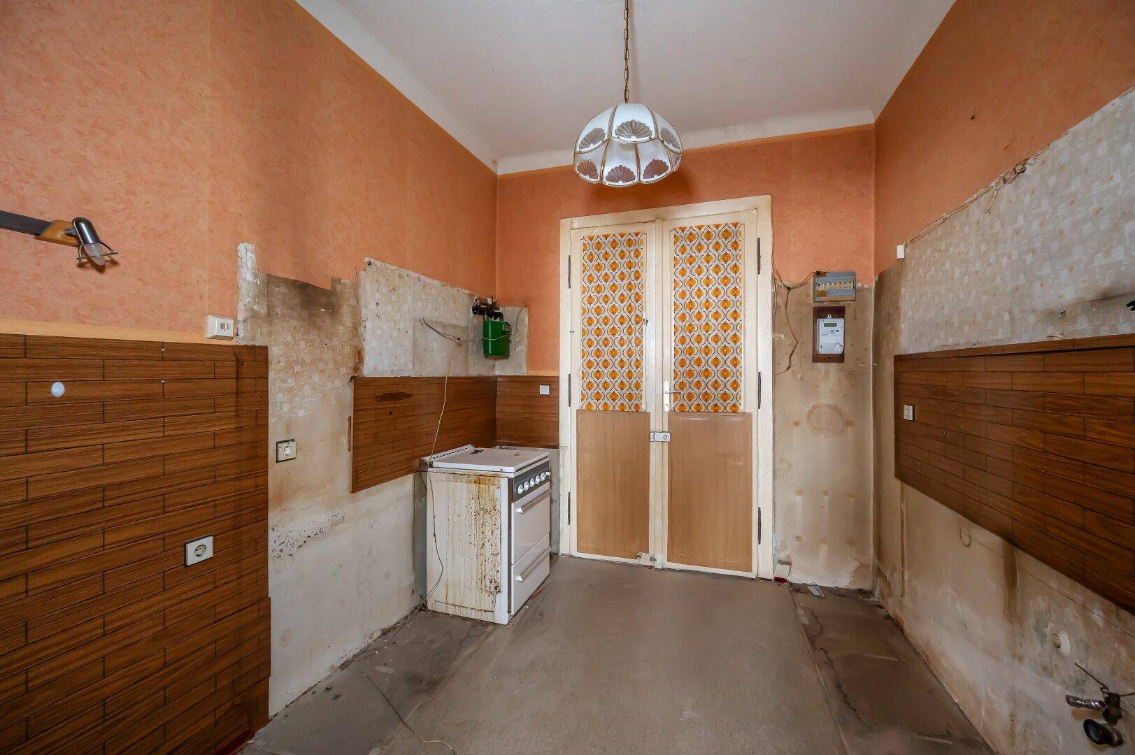Renovierungsbedürftige Küche mit altem Herd, orangefarbenen Wänden und freiliegenden Installationen.