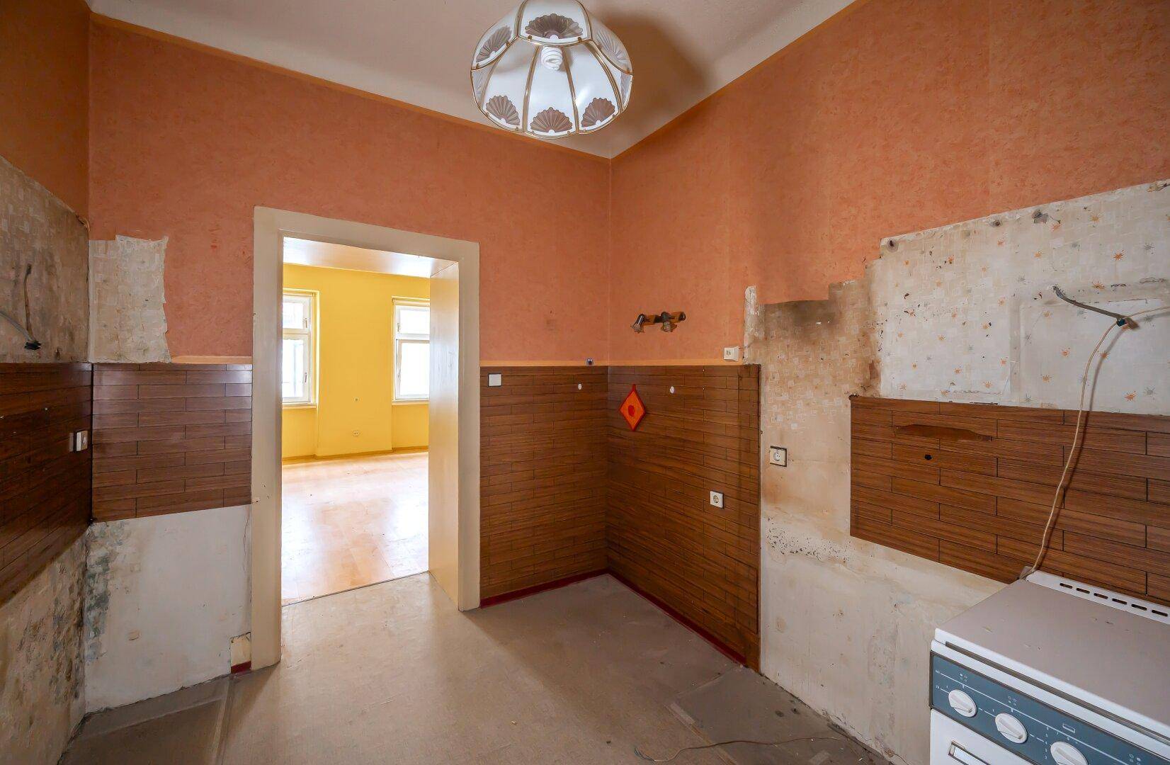 Renovierungsbedürftige Küche mit orangefarbenen Wänden und Blick in ein angrenzendes Zimmer.