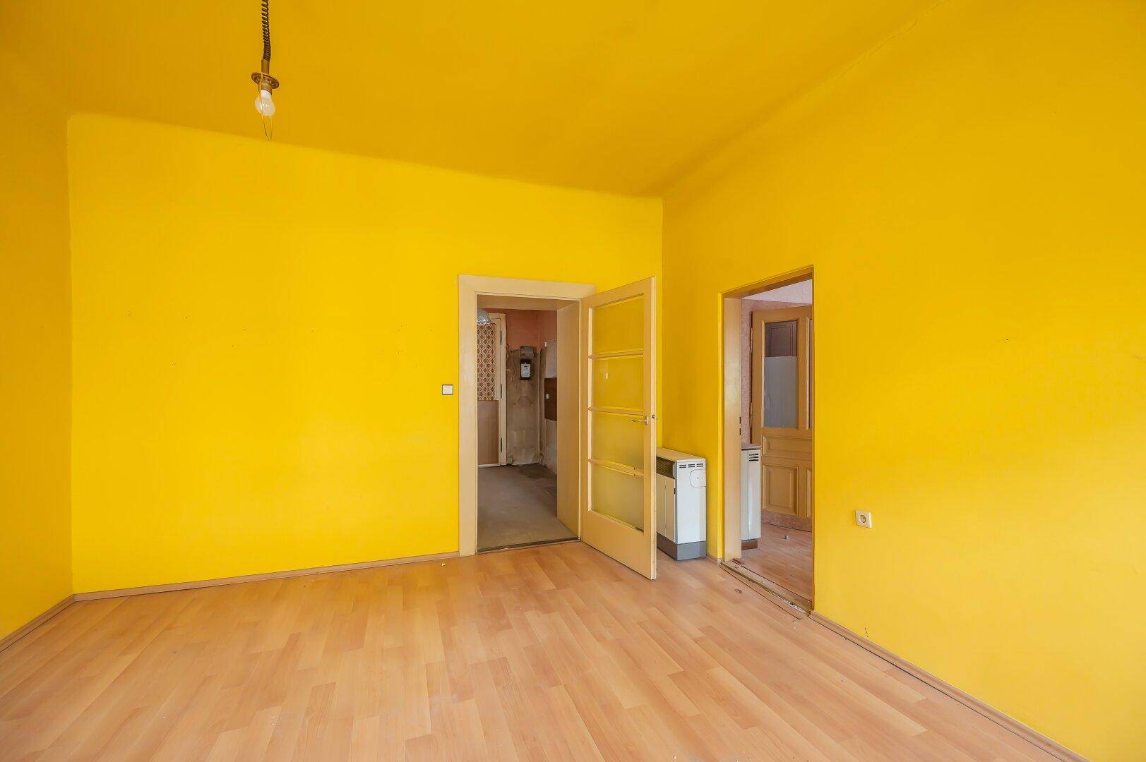 Helles Zimmer mit gelben Wänden, Laminatboden und Zugang zu weiteren Räumen.
