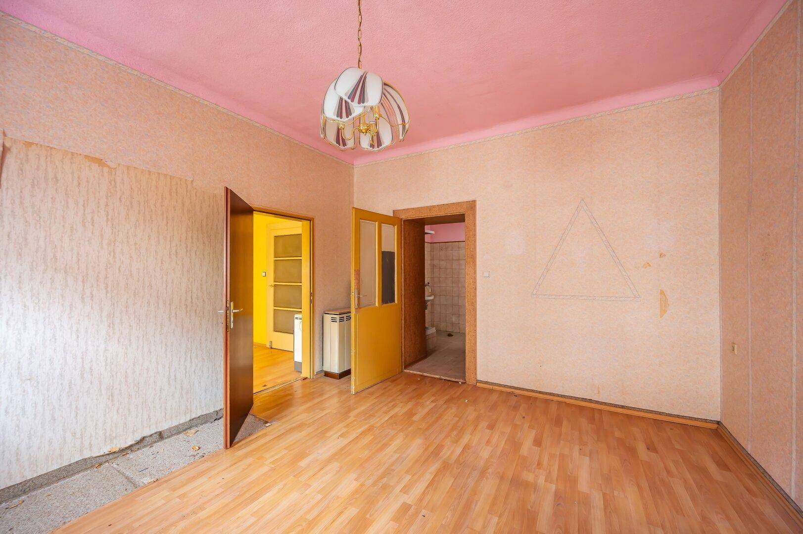 Leeres Zimmer mit Laminatboden, rosa Decke und renovierungsbedürftigen Wänden.