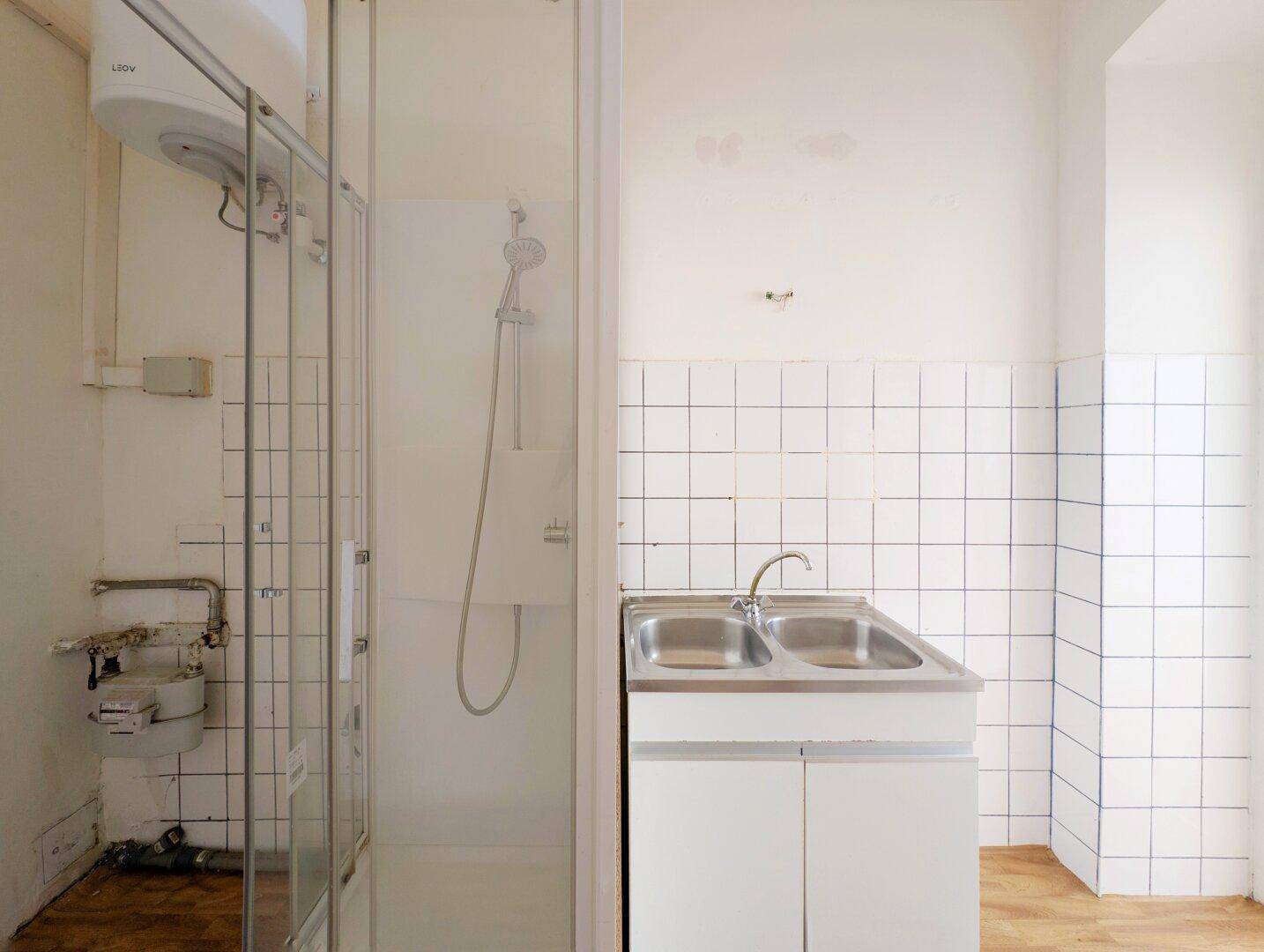 Kleines Badezimmer mit Duschkabine, Doppelwaschbecken und weiß gefliesten Wänden.