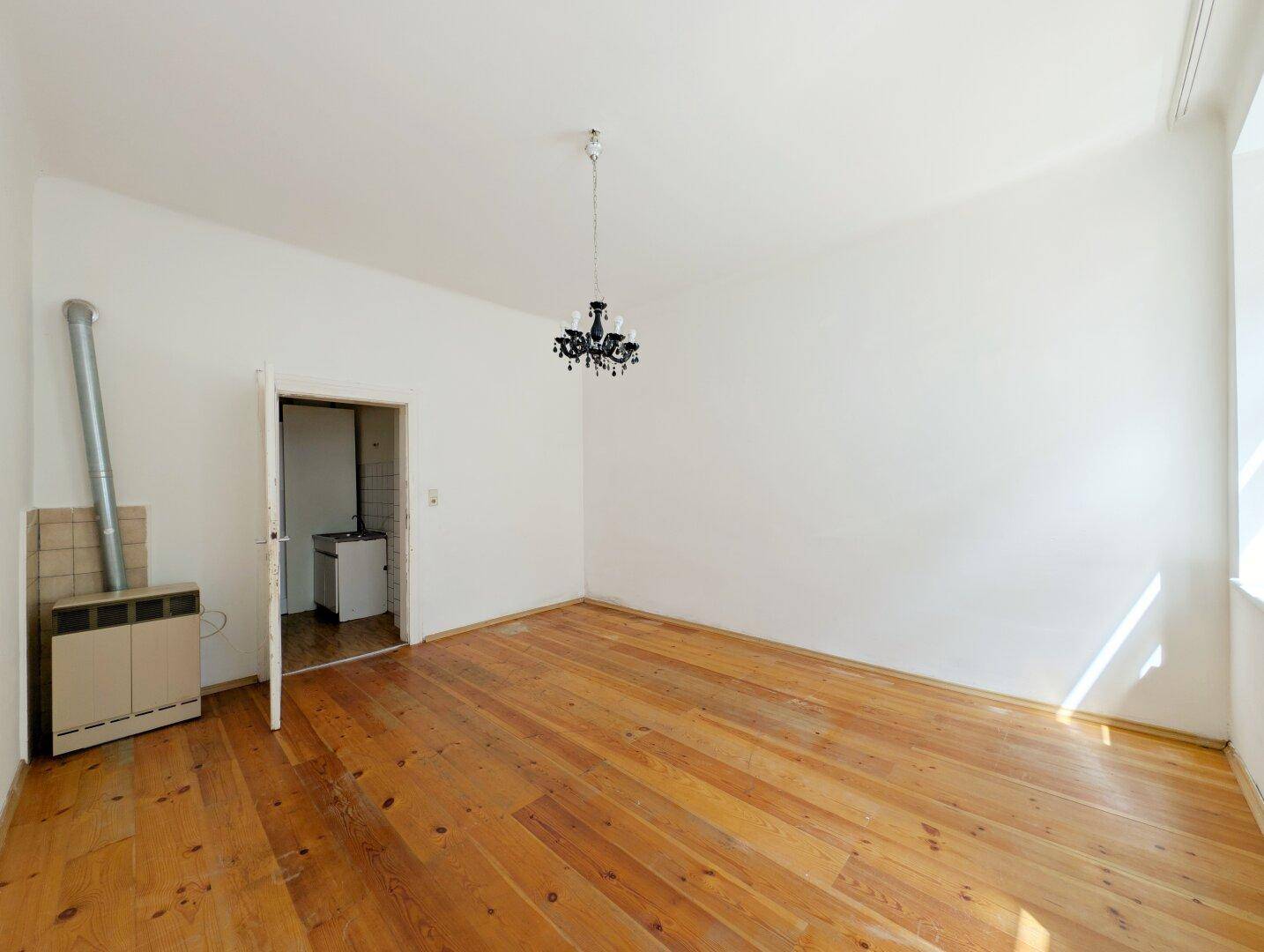 Heller Raum mit Holzdielenboden, Kronleuchter und offenem Zugang zu einem Nebenraum.