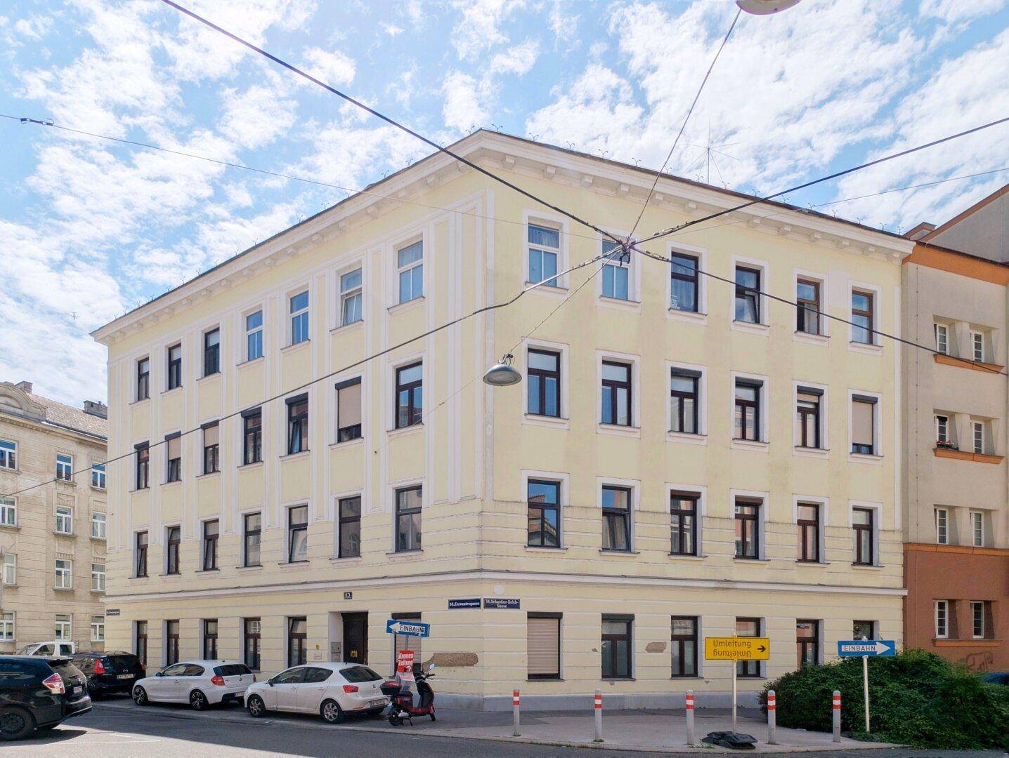 Gelbes Eckgebäude mit vielen Fenstern und klassischer Architektur in städtischer Umgebung.