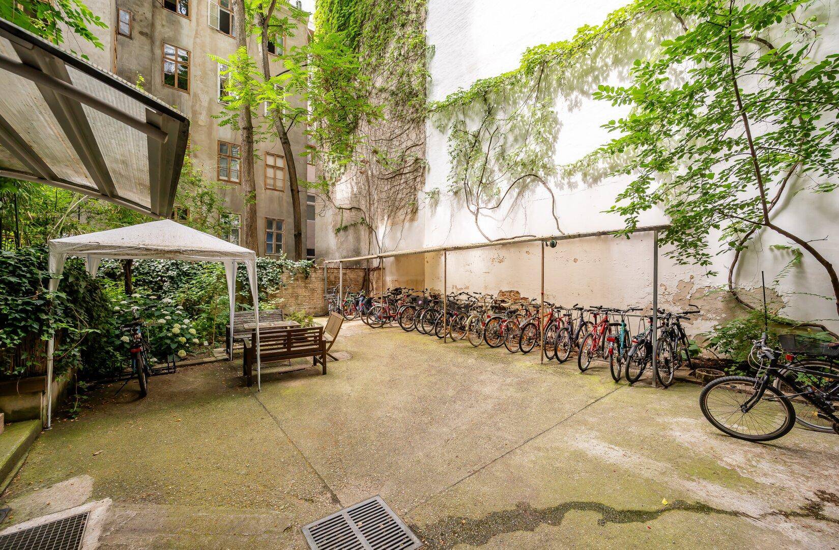 Großer begrünter Innenhof mit vielen Fahrrädern, einem Pavillon und einer Sitzbank.