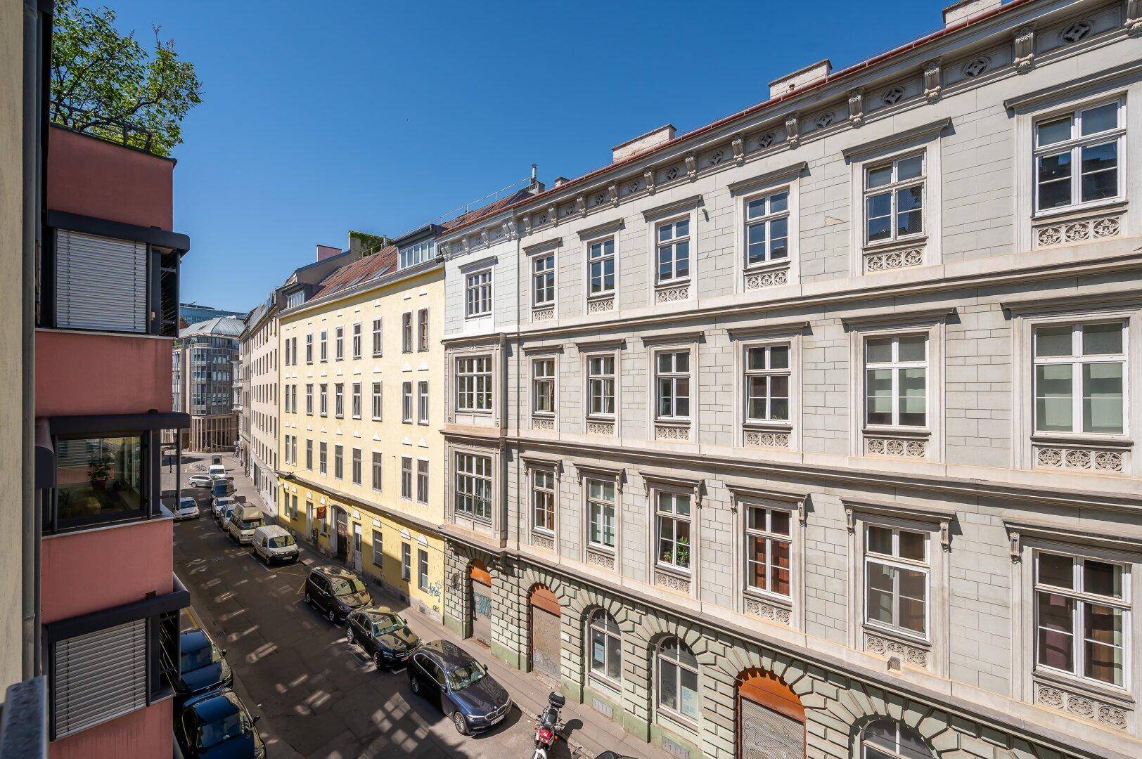 Blick auf eine belebte Straße mit parkenden Autos und historischen Gebäudefassaden.
