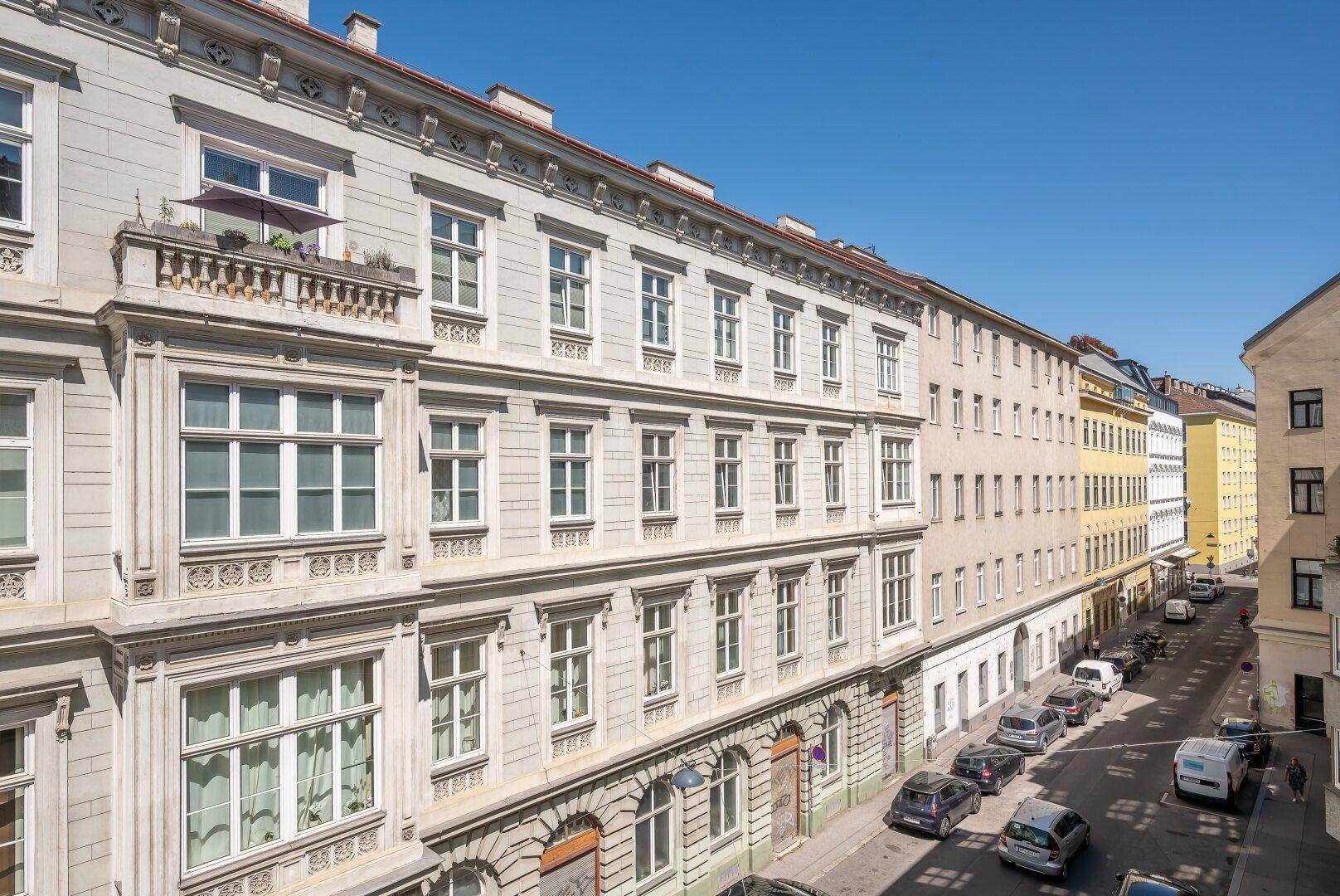 Weitläufiger Blick auf eine städtische Straße mit geparkten Fahrzeugen und Altbauten.