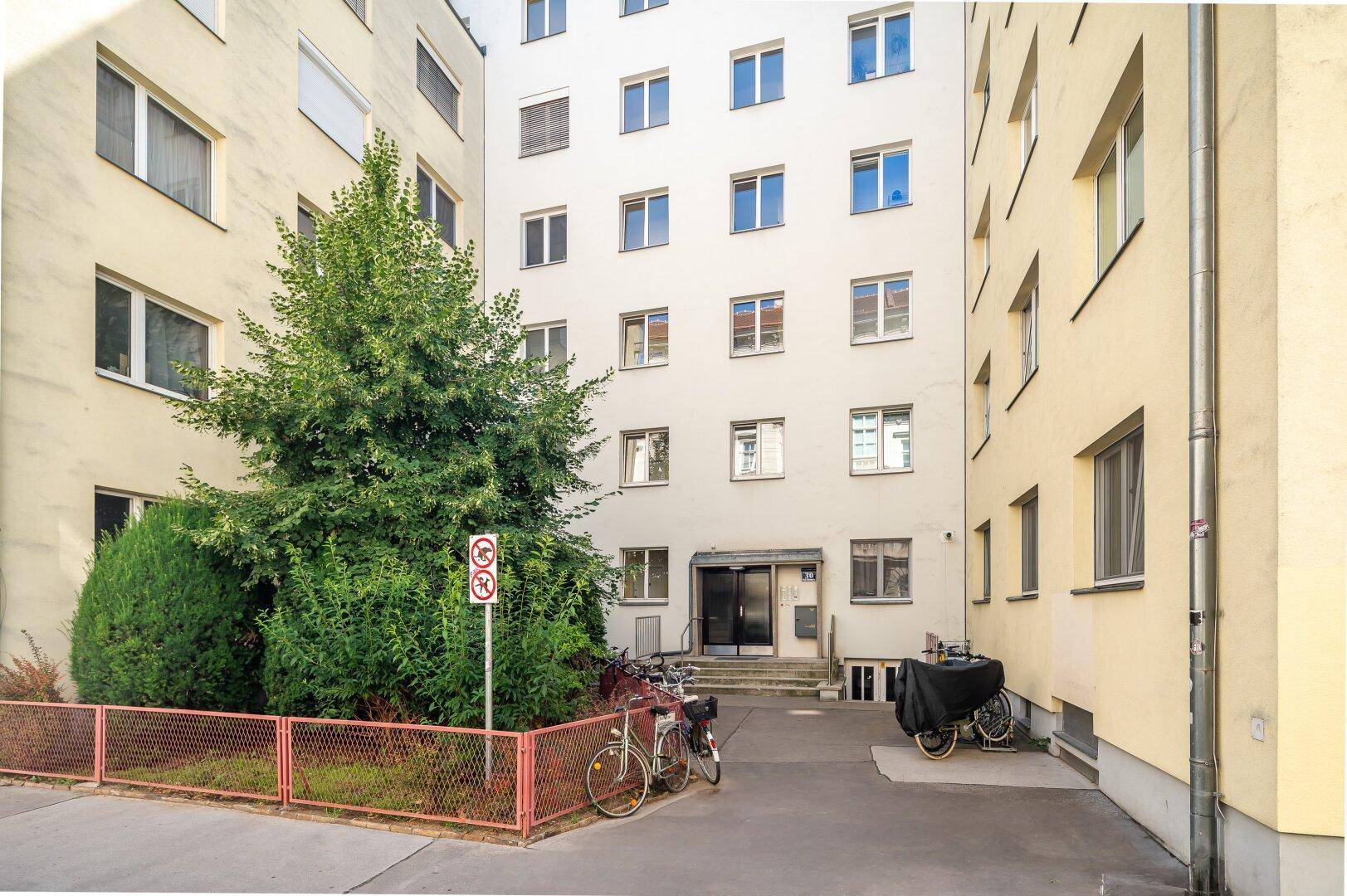 Eingangsbereich eines Wohngebäudes mit geparkten Fahrrädern und umliegenden Fassaden.