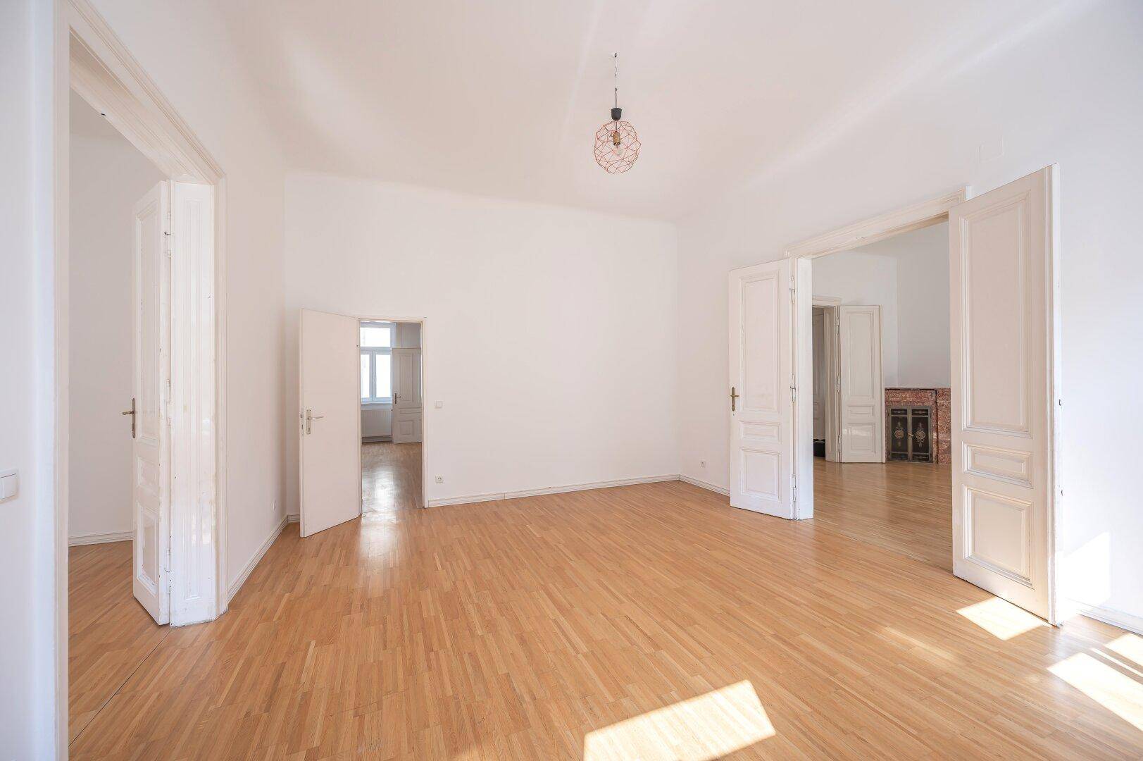 Großes, leeres Zimmer mit Holzboden, hohen Türen und viel Potenzial zur Gestaltung.