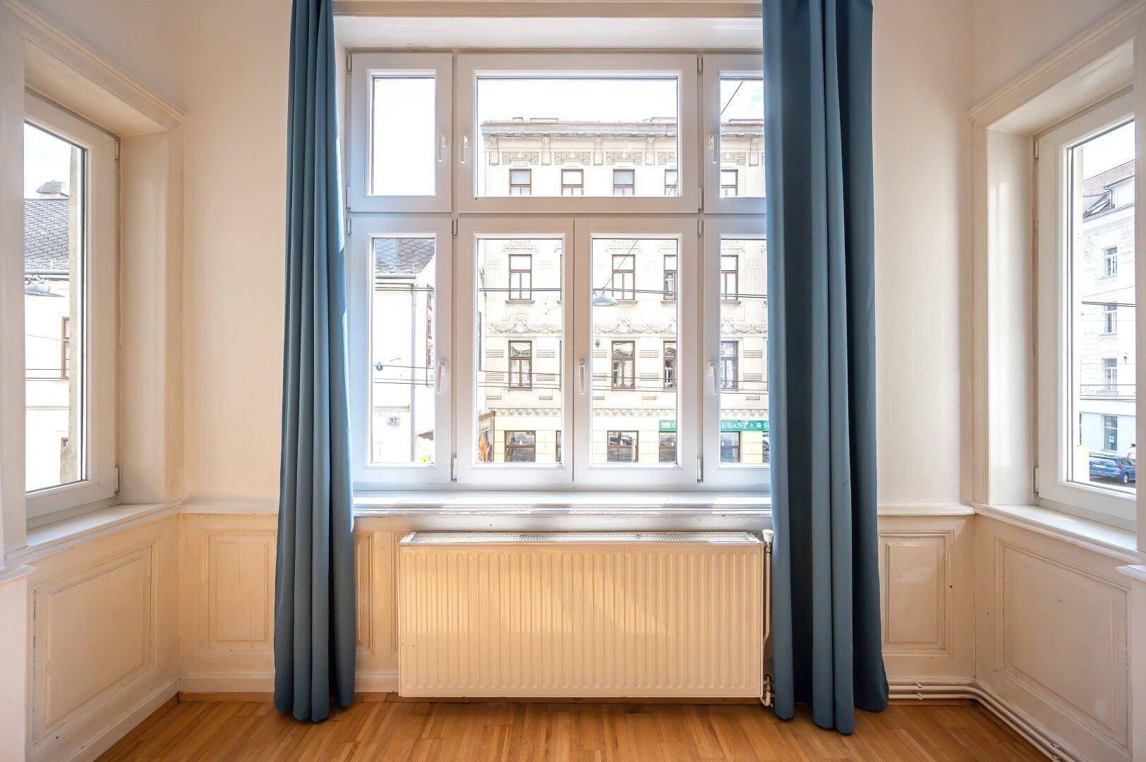 Großes Fenster mit blauen Vorhängen und Blick auf die gegenüberliegenden Gebäude.
