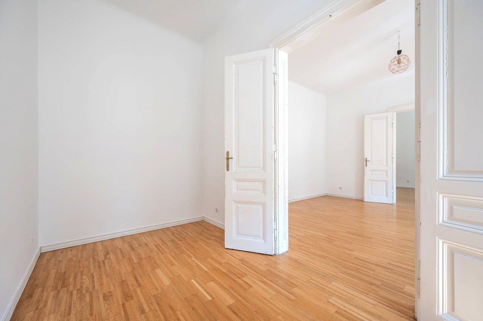 Leeres Zimmer mit Holzboden und hohen weißen Türen, bereit zur individuellen Einrichtung.