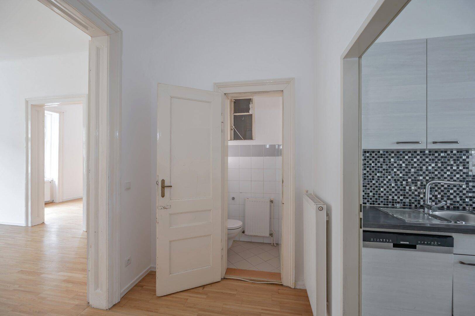 Kleines WC mit Fliesenboden, weißer Toilette und Heizkörper, funktional eingerichtet.