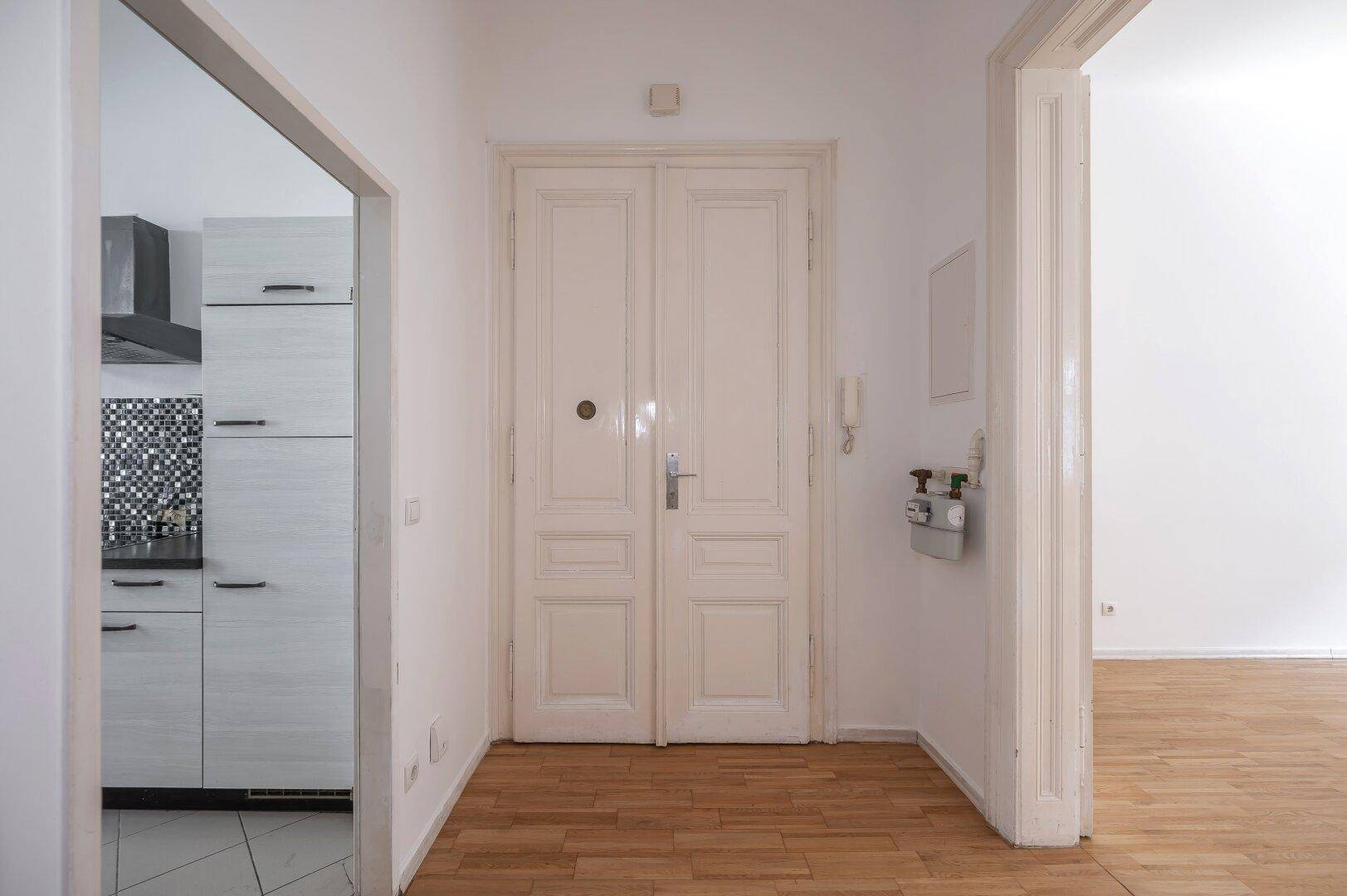 Eingangsbereich mit Holzboden und hohen Doppeltüren, die zur Wohnung führen.