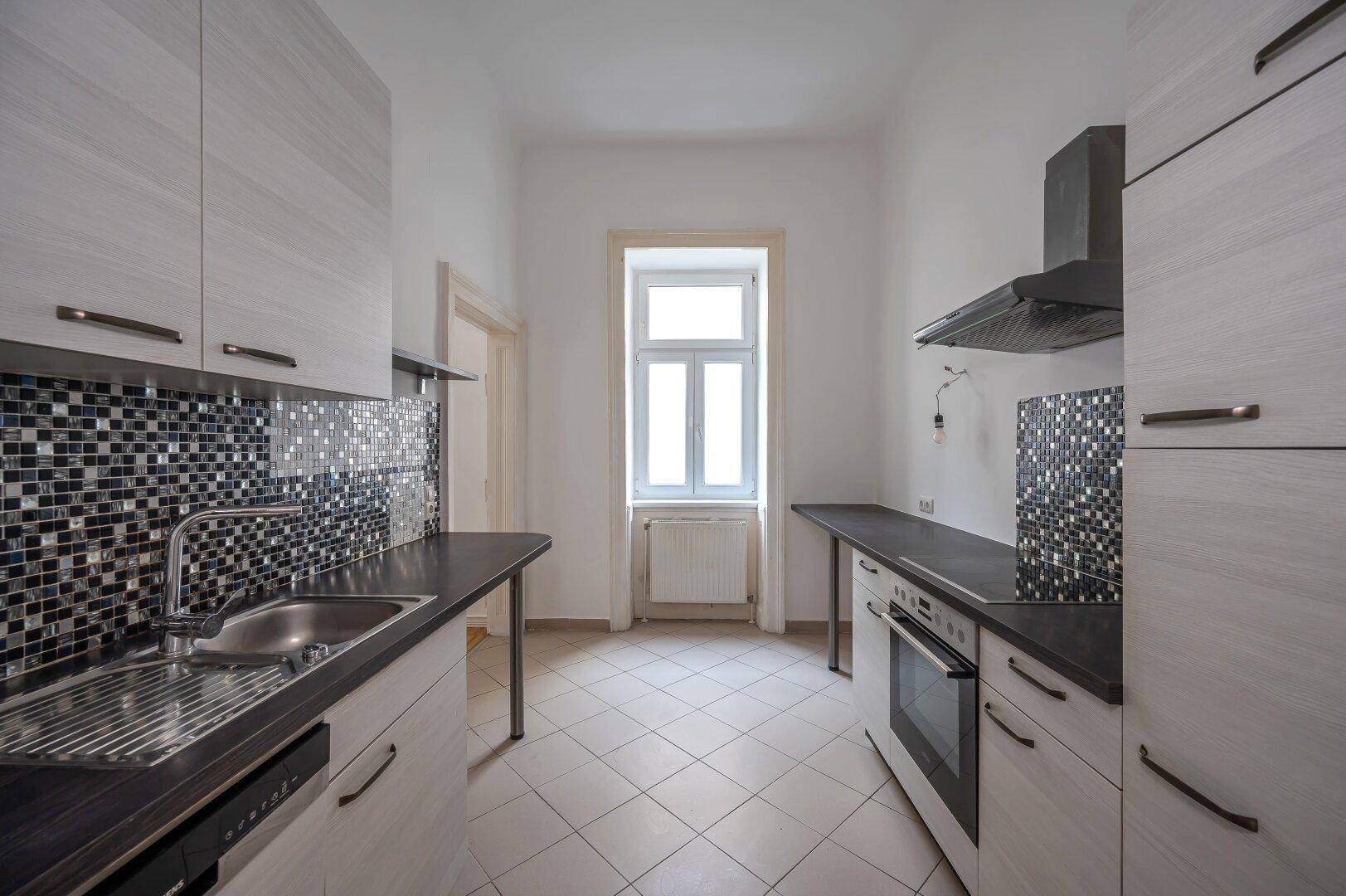 Moderne Küche mit Fliesenboden, dunklen Arbeitsplatten und integrierten Geräten.