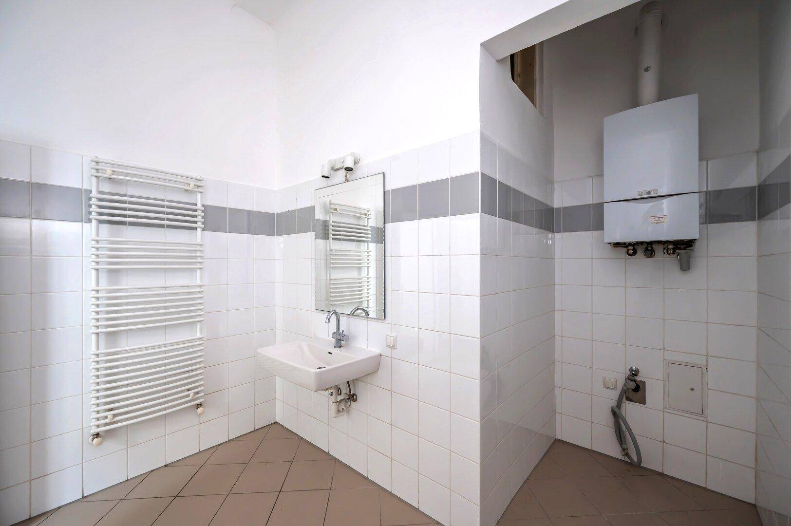 Badezimmer mit Fliesenboden, Waschbecken, Handtuchheizkörper und Warmwasserboiler.