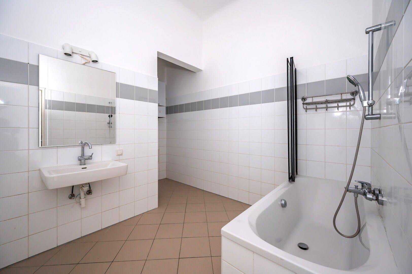 Badezimmer mit Fliesenboden, Badewanne und Waschbecken, hell und funktional.