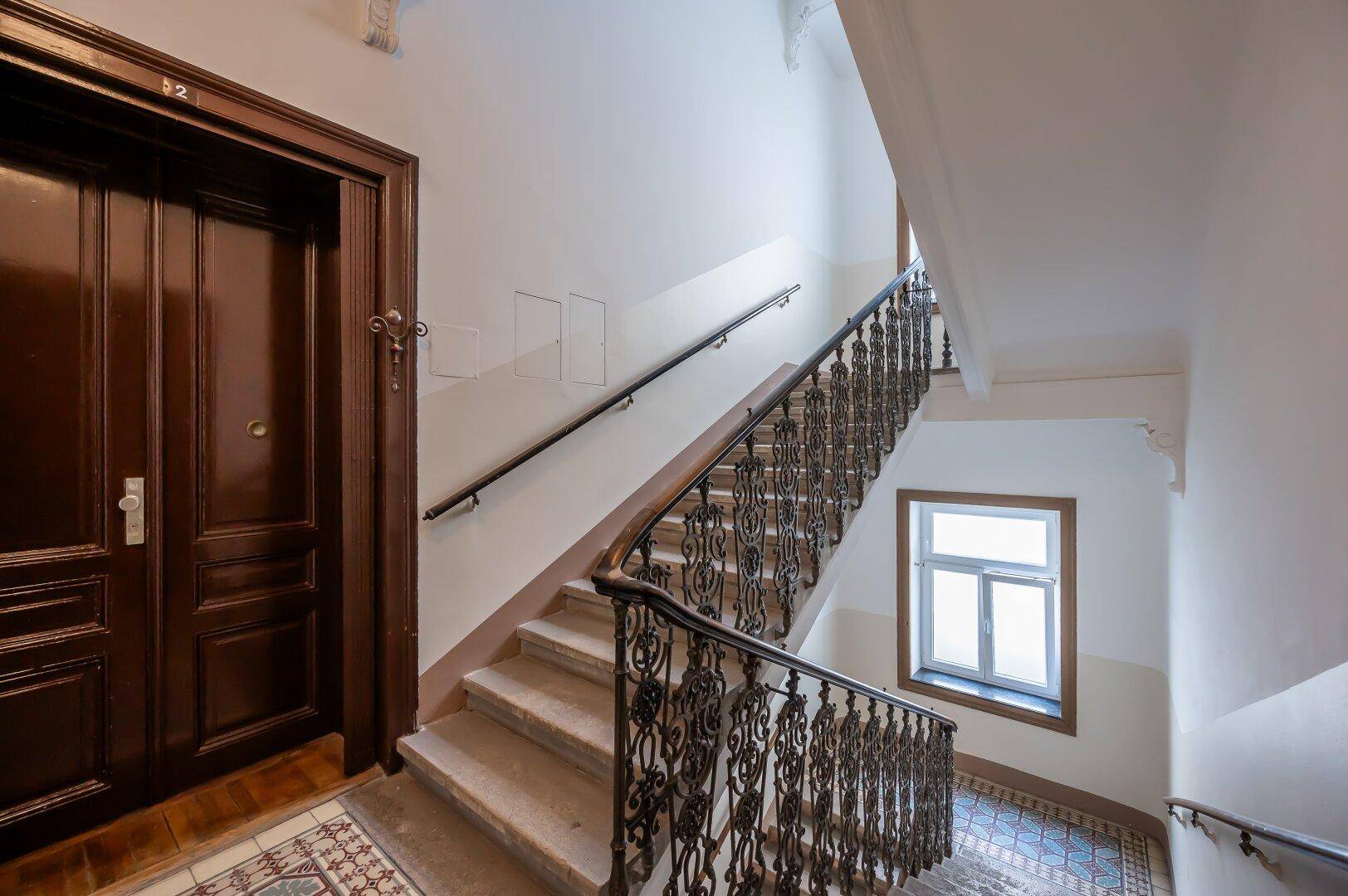 Historisches Treppenhaus mit schmiedeeisernem Geländer und verzierten Details.