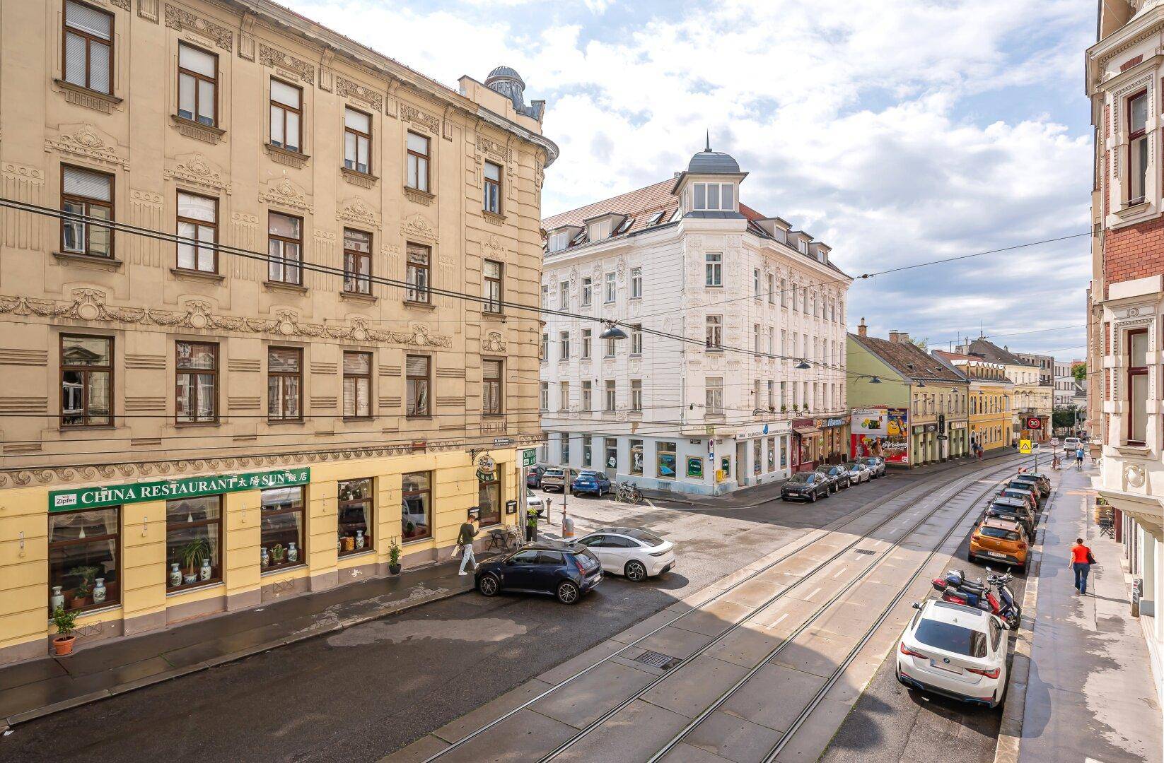 Stadtansicht mit historischen Gebäuden, Geschäften und geparkten Autos entlang der Straße.