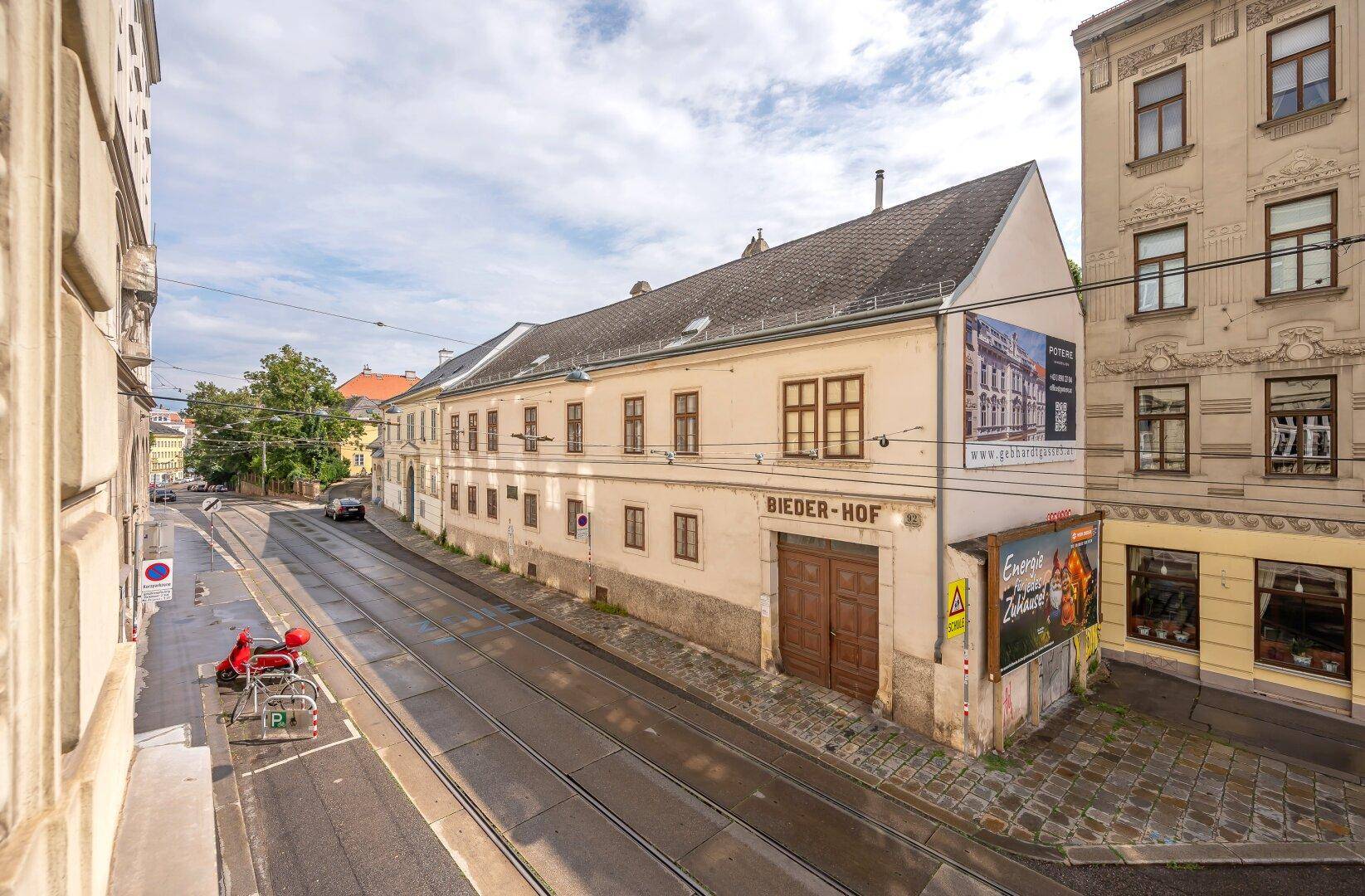 Historisches Gebäude an einer Straße mit Straßenbahnschienen und umliegenden Häusern.
