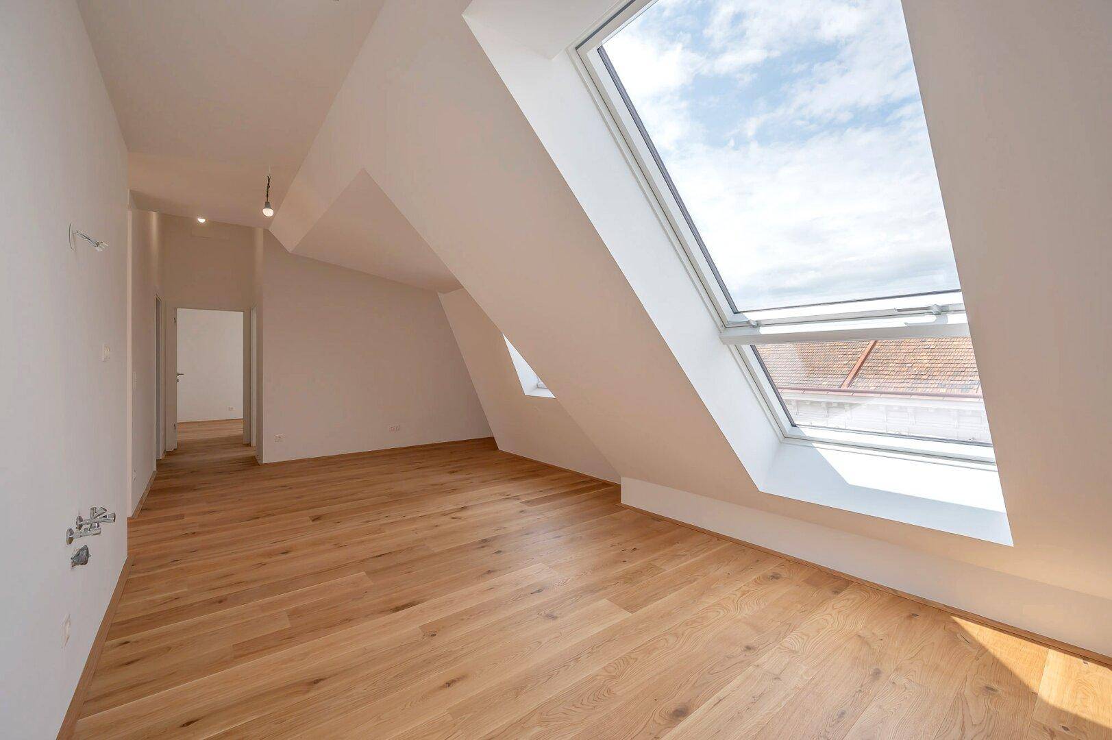Lichtdurchfluteter Raum mit Holzboden, Dachschrägen und mehreren Dachfenstern.