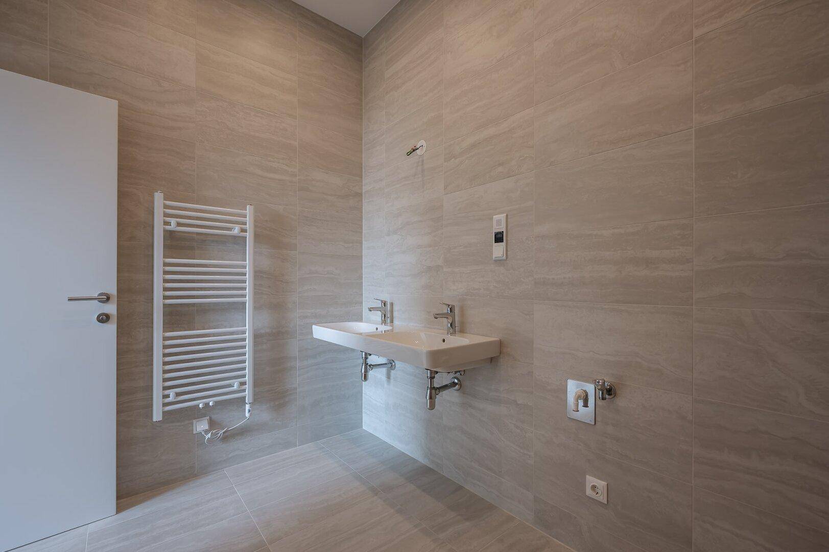 Geräumiges Badezimmer mit Doppelwaschbecken, Handtuchheizkörper und modernen Fliesen.