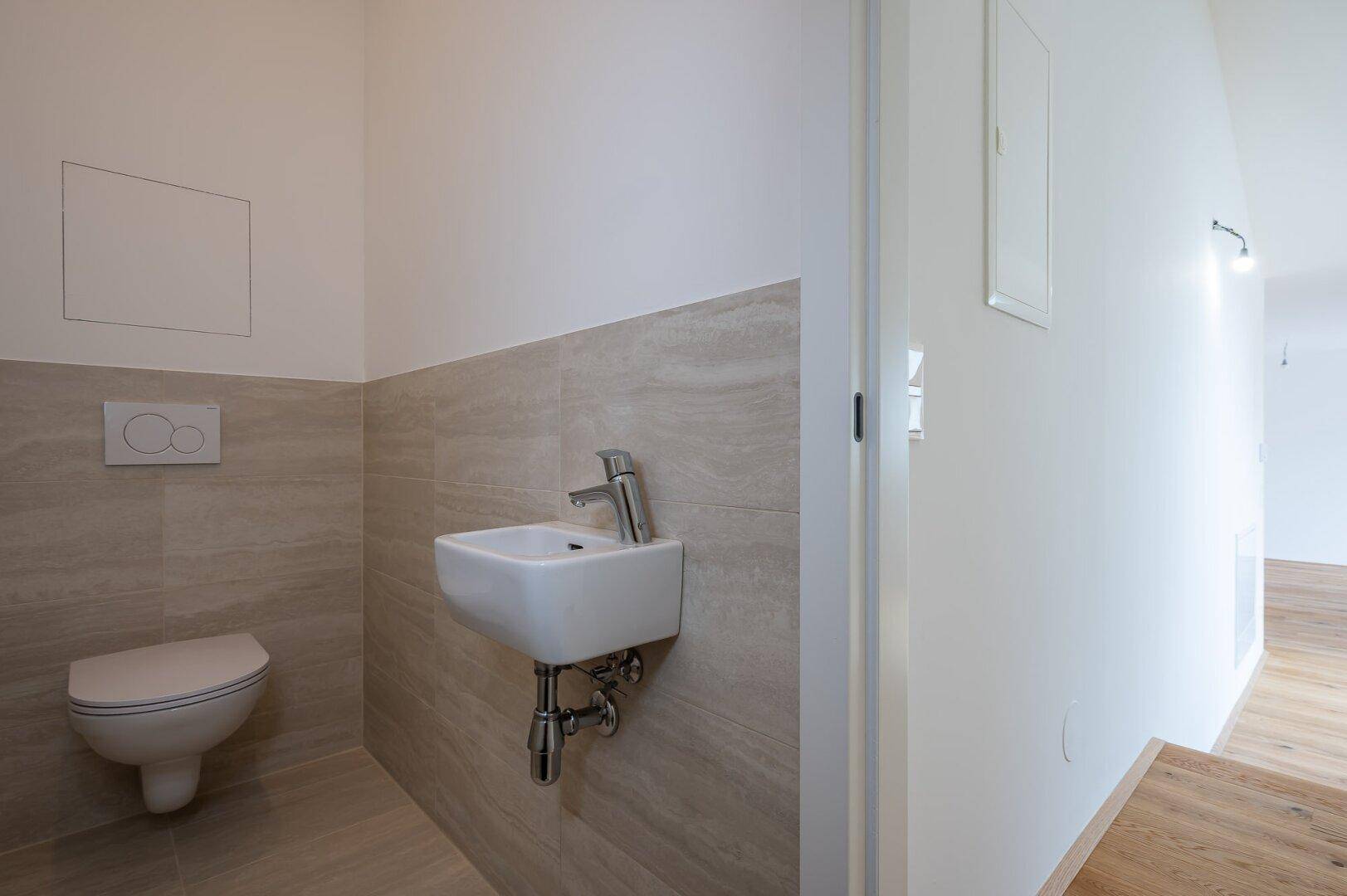 Modernes Gäste-WC mit Wand-WC, kleinem Waschbecken und hellen Fliesen.