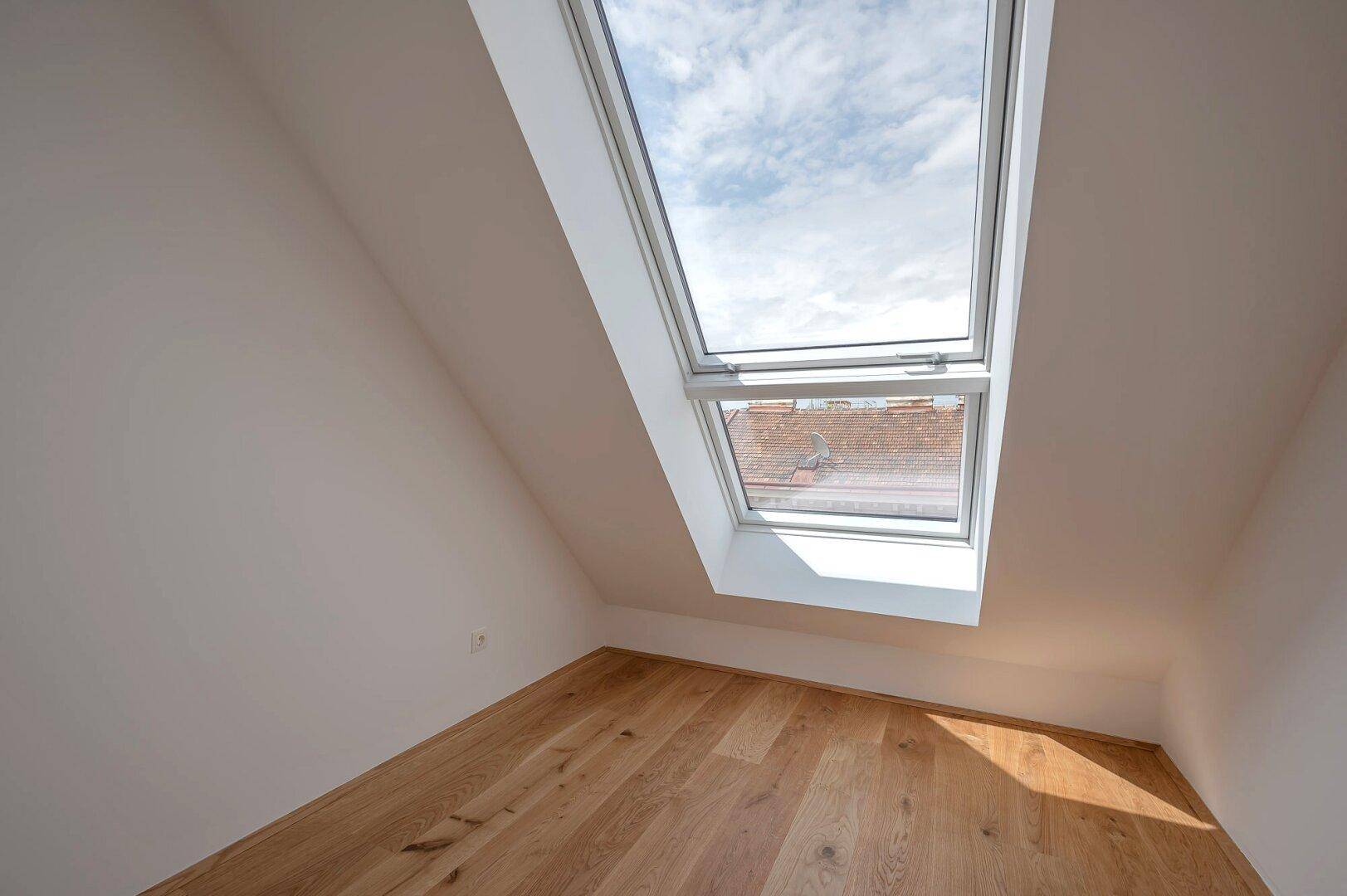 Gemütliches Schlafzimmer mit Holzboden, Dachschräge und großem Dachfenster.