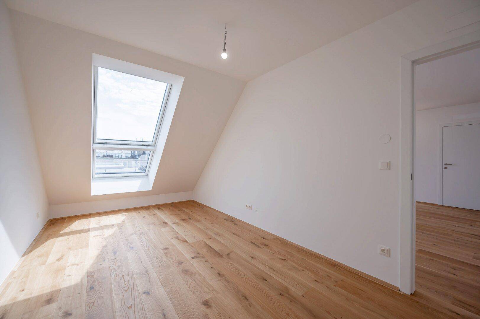 Geräumiges Schlafzimmer mit Holzboden, Dachschräge und einem großen Dachfenster.
