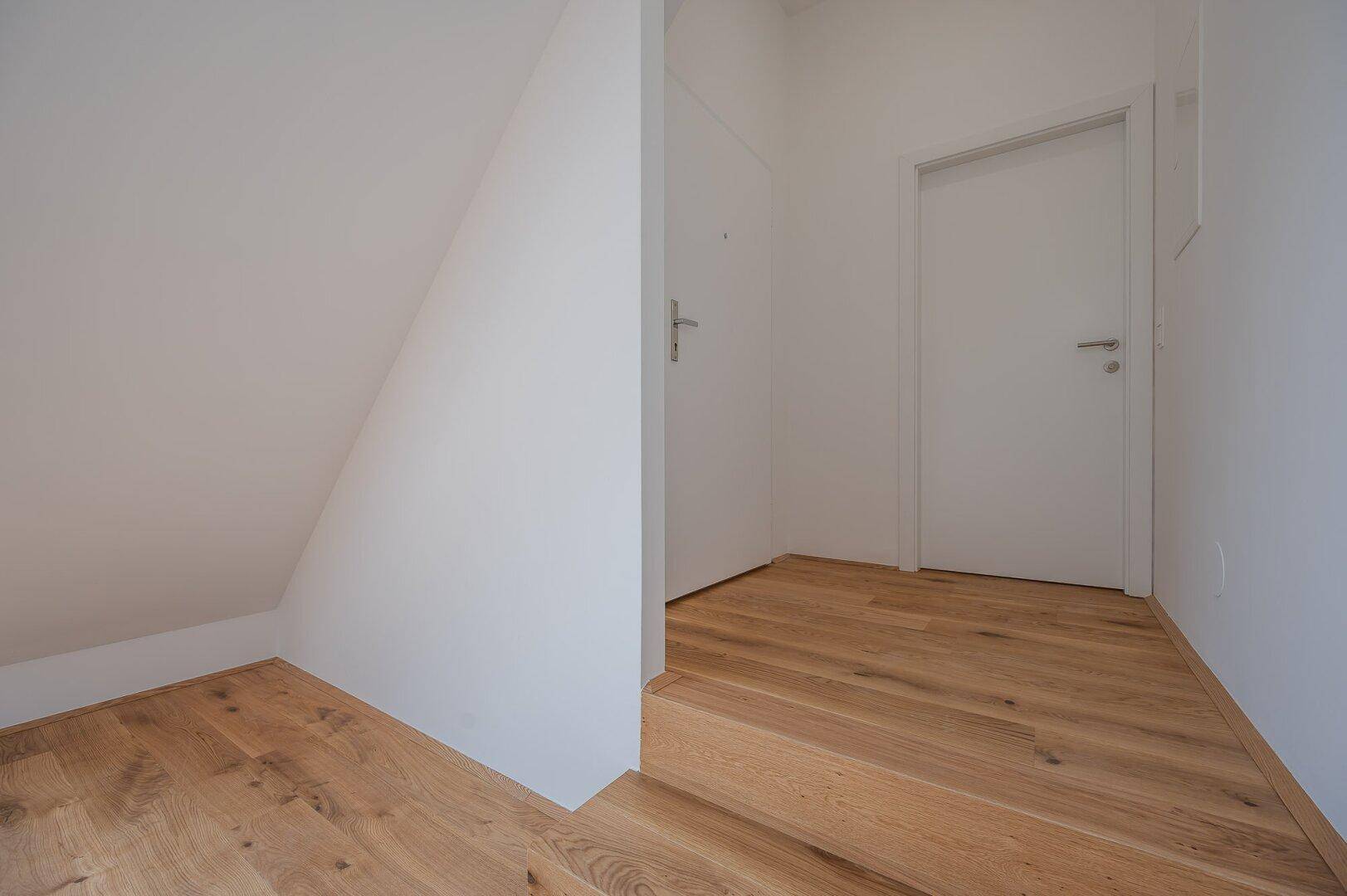 Heller Flurbereich mit Holztreppe, weißen Türen und schrägen Wänden im Dachgeschoss.