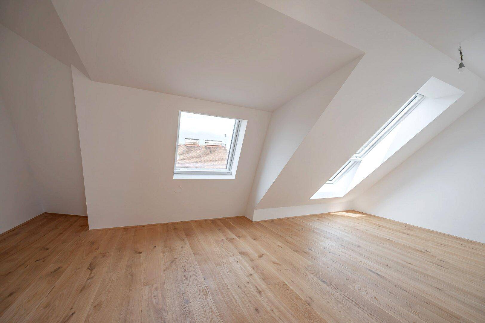 Offener Wohnbereich mit Holzboden, Dachschrägen und mehreren Dachfenstern für viel Licht.