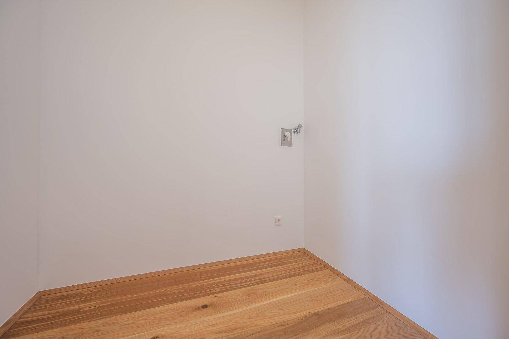 Kleiner, heller Eckbereich mit Holzboden und weißen Wänden, ideal als Abstellfläche.
