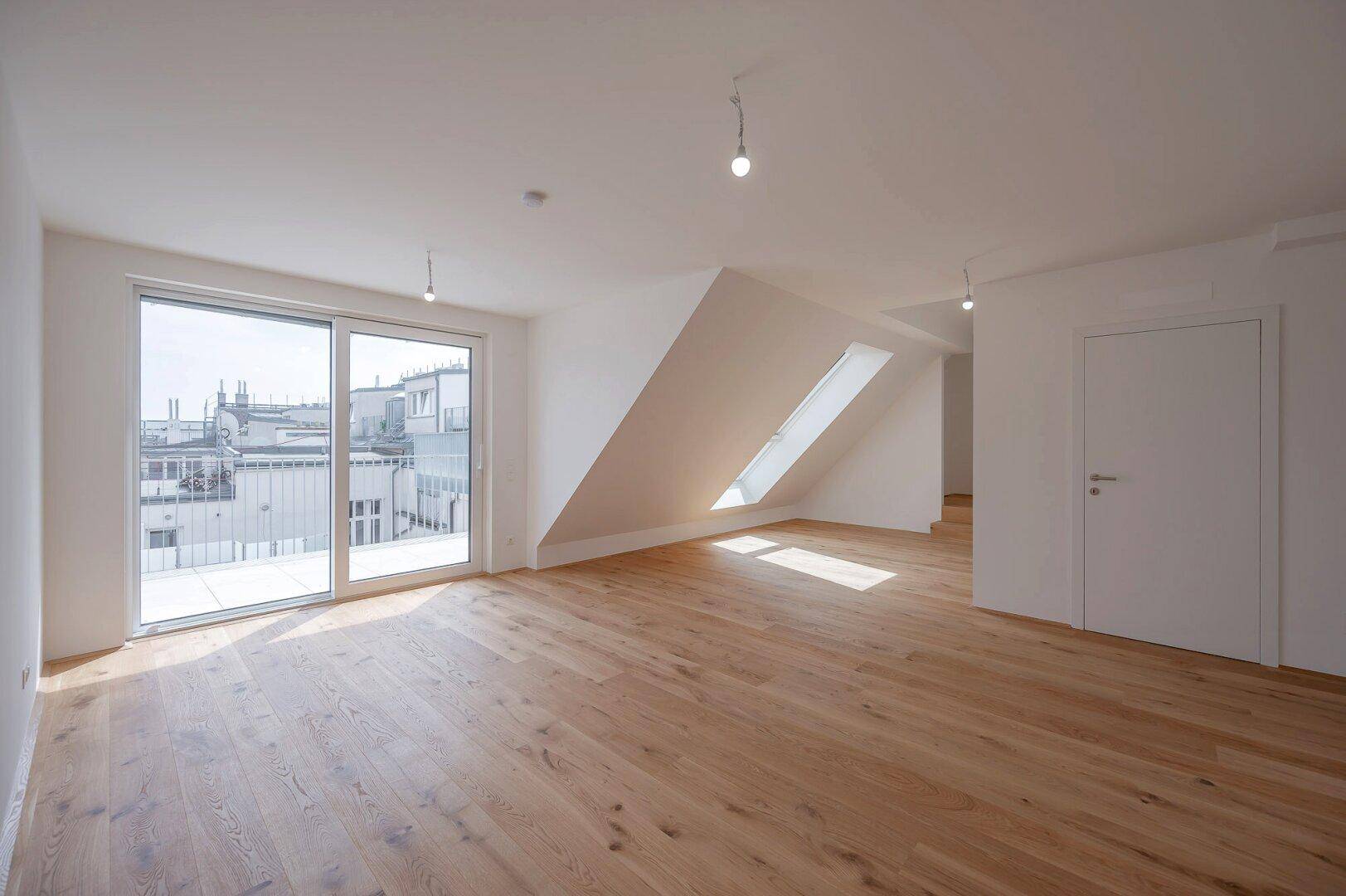 Heller Wohnraum mit Eichenparkett, Dachschrägen und Zugang zu einem Balkon.