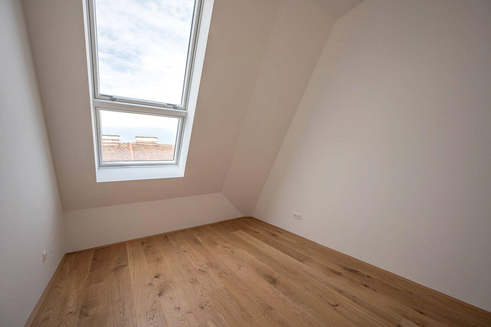 Ruhiges Schlafzimmer mit Holzboden, Dachschräge und einem großen Dachfenster.