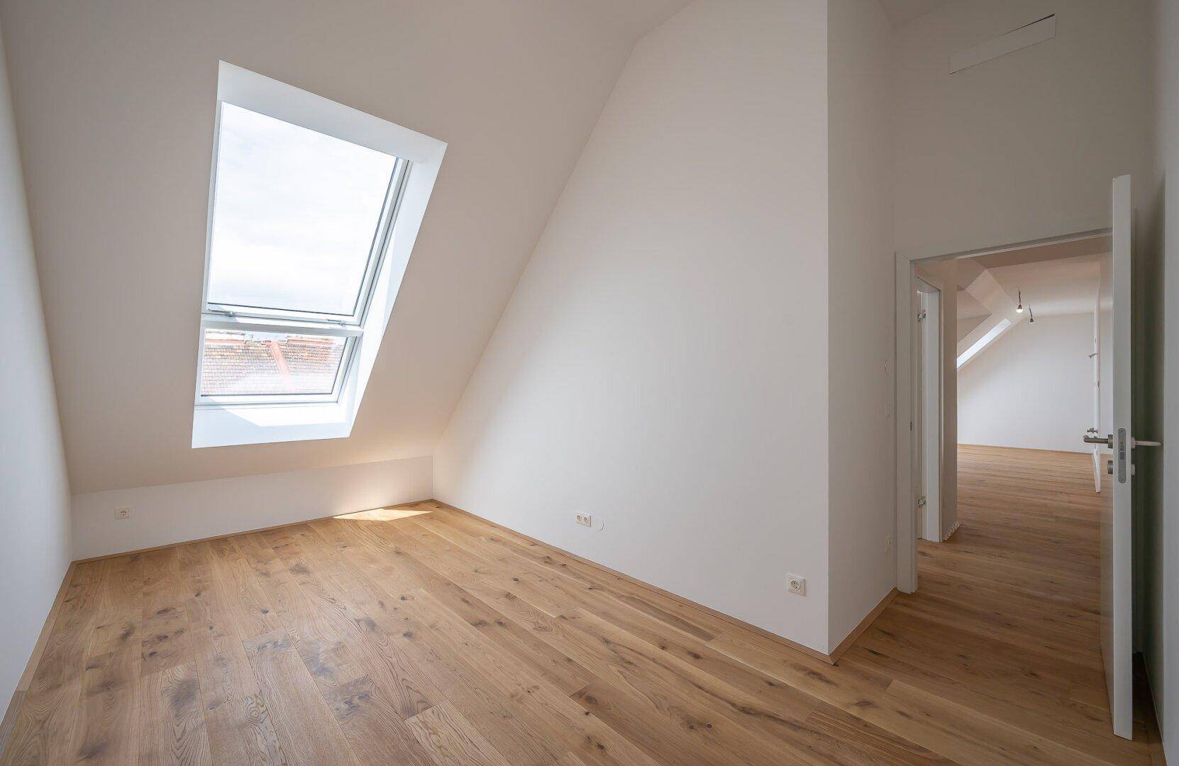 Helles Schlafzimmer mit Holzboden, Dachschräge und großem Dachfenster, offen zum Flur.