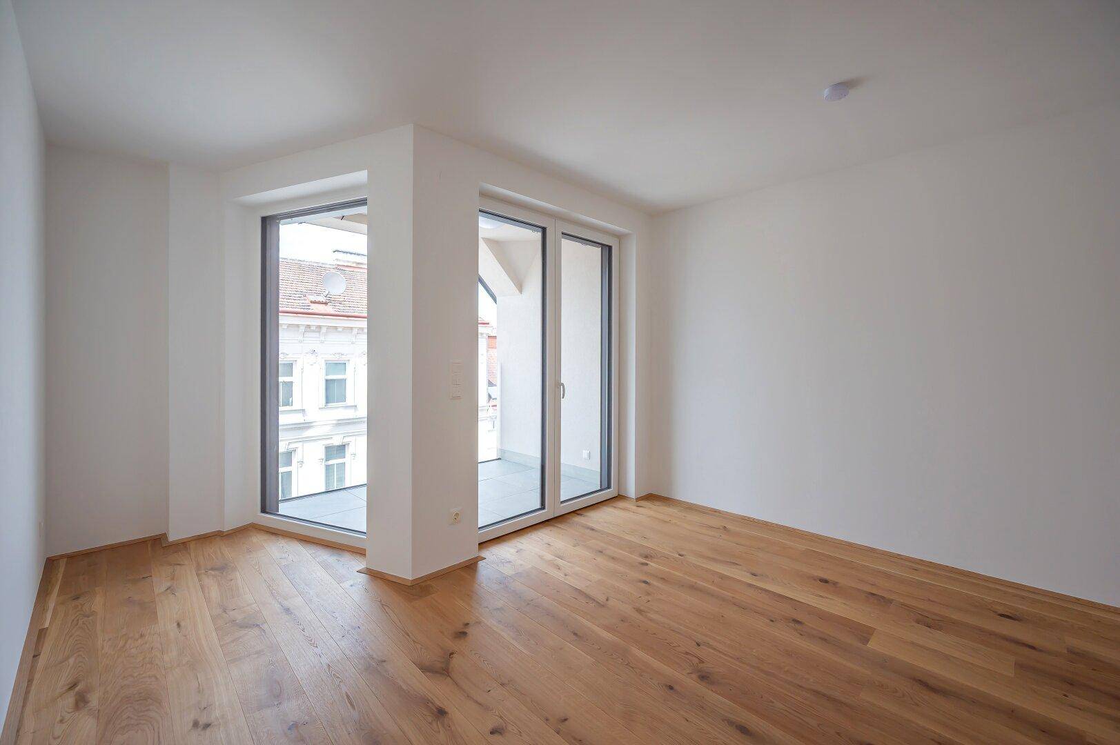 Eckzimmer mit Holzboden und großen Fenstern, die viel Licht und einen weiten Blick ermöglichen.