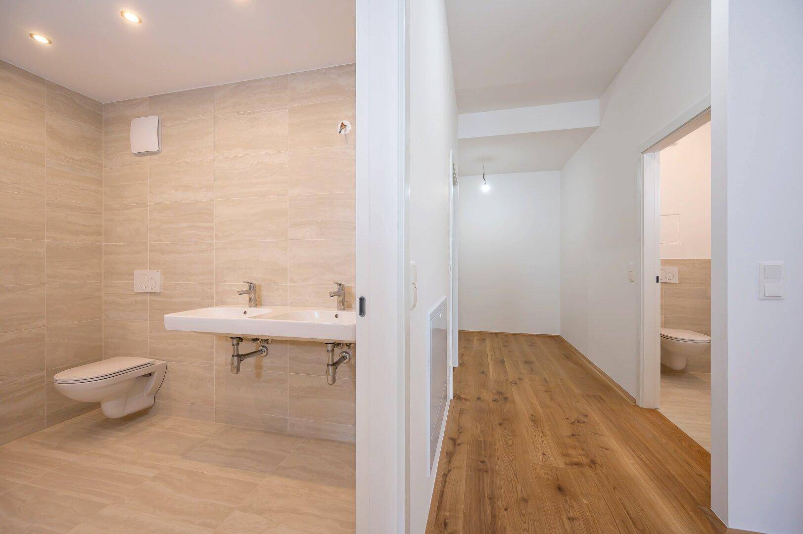 Heller Flur mit Parkettboden, der zu einem modernen Badezimmer mit Doppelwaschbecken und separatem WC führt.