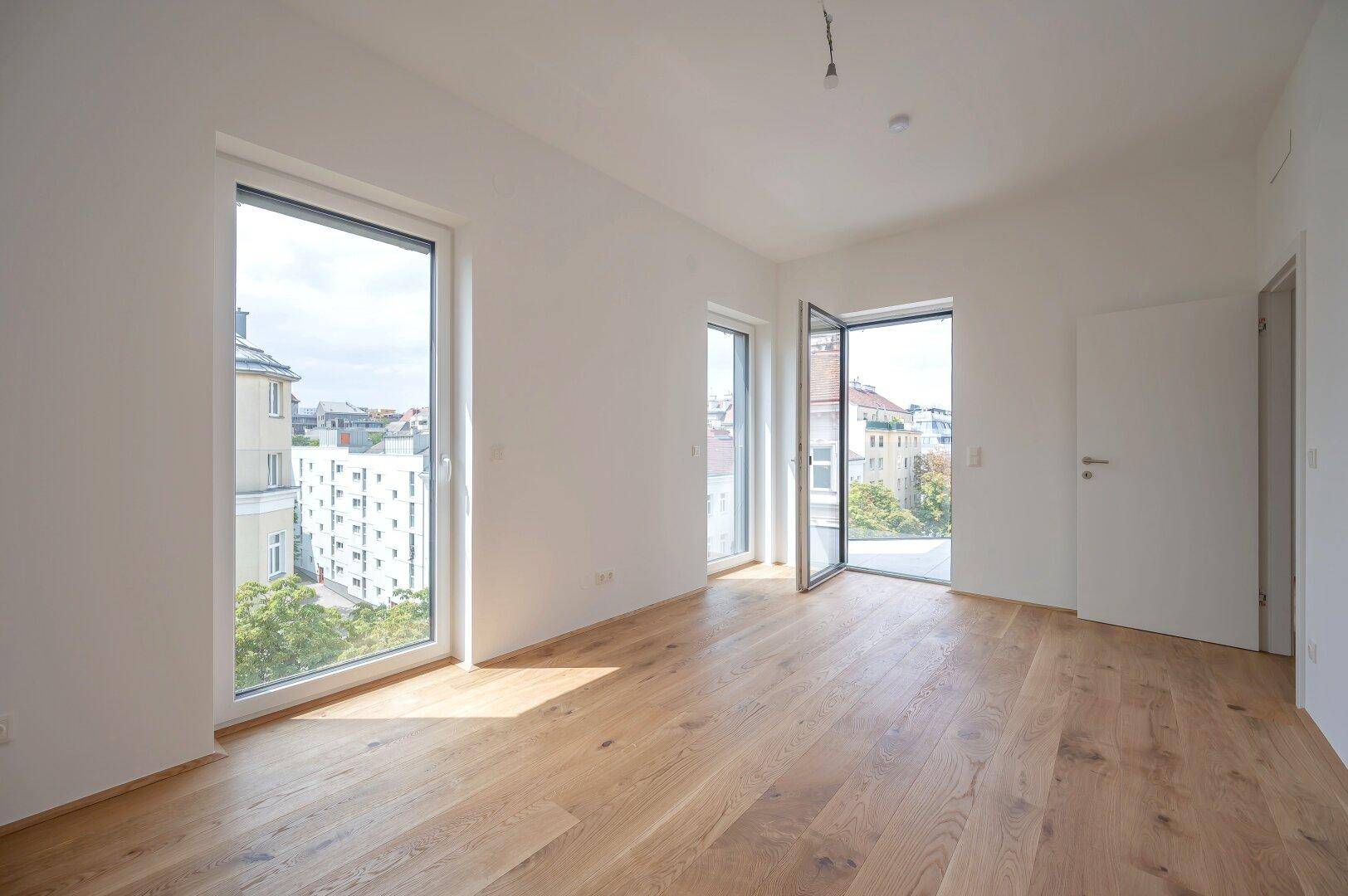 Geräumiges, helles Zimmer mit Holzboden und großen Fenstern, die einen weiten Blick auf die Stadt bieten.