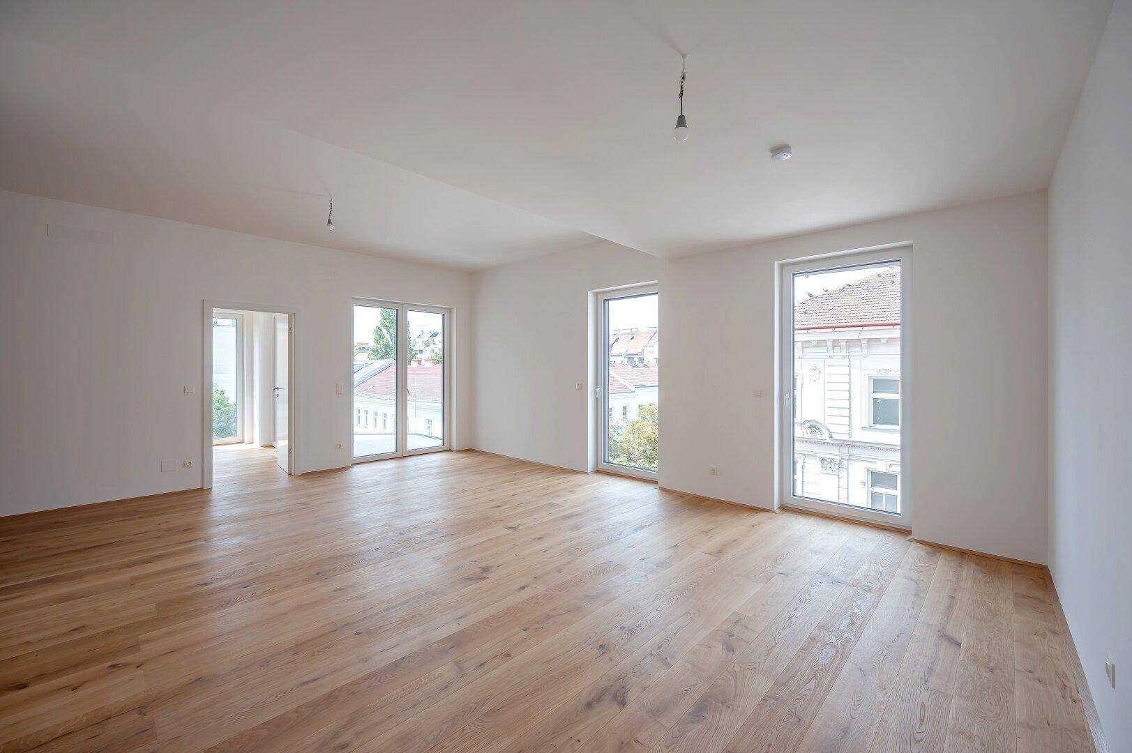 Geräumiges, helles Zimmer mit Holzboden und mehreren Fenstern, die viel Tageslicht hereinlassen.