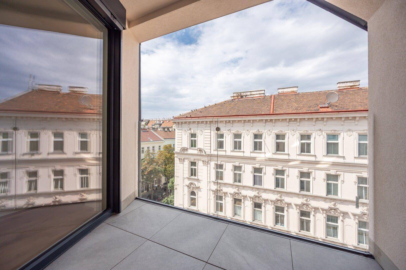 Moderner Balkon mit Fliesenboden und Blick auf die umliegenden Gebäude.