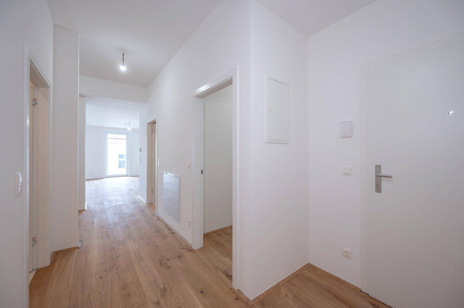 Heller Flur mit Holzboden und weißen Wänden, der zu weiteren Räumen führt.
