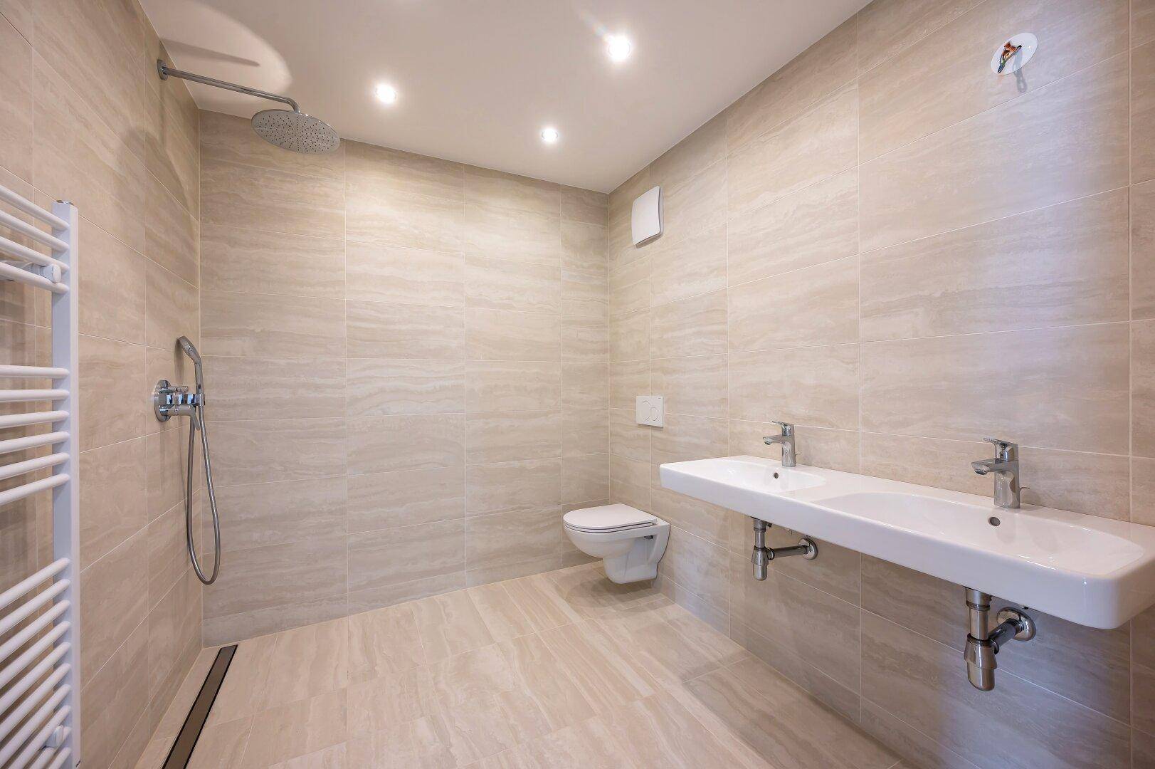 Modernes Badezimmer mit begehbarer Dusche, Doppelwaschbecken und beigefarbenen Fliesen.