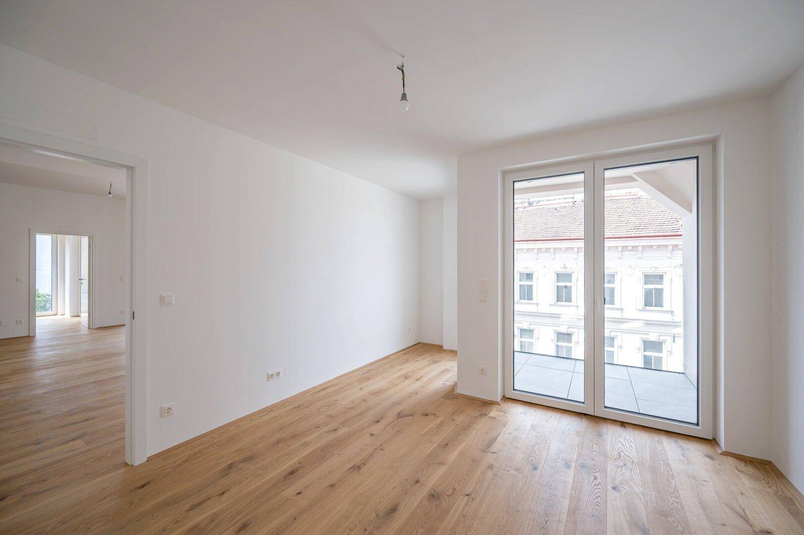 Geräumiges Zimmer mit Parkettboden und großen Fenstern mit Blick auf die Stadt.