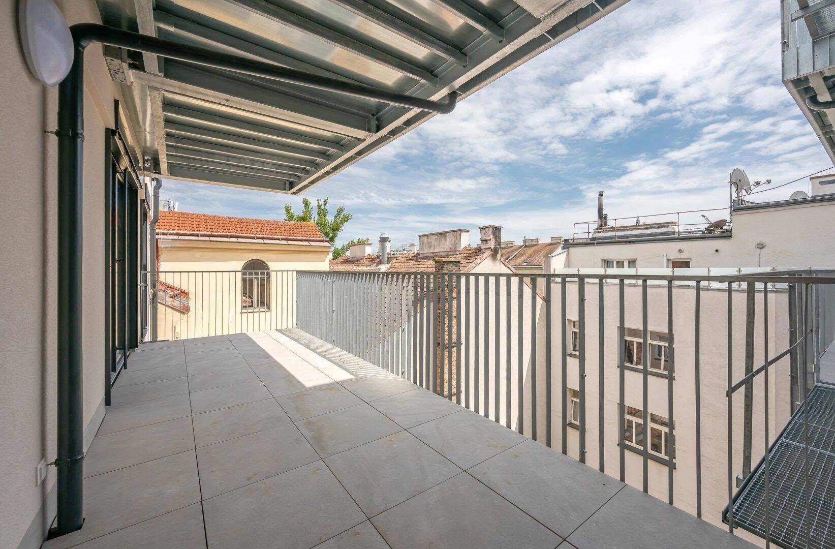 Heller Balkon mit Fliesenboden und Blick auf die umliegenden Gebäude und Dächer.