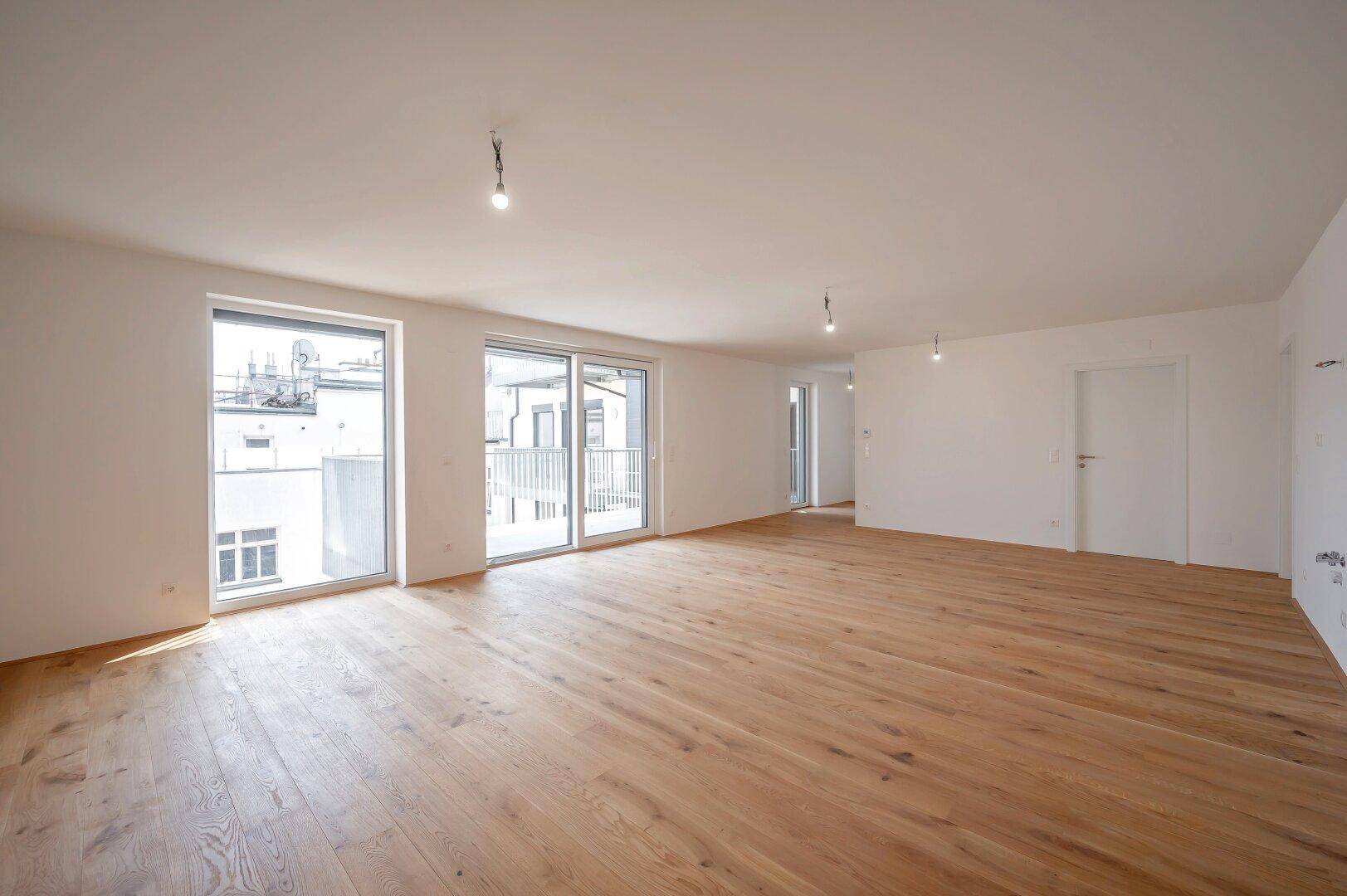 Heller, leerer Wohnbereich mit neuem Holzparkett und Zugang zum Balkon, bereit zur Gestaltung.