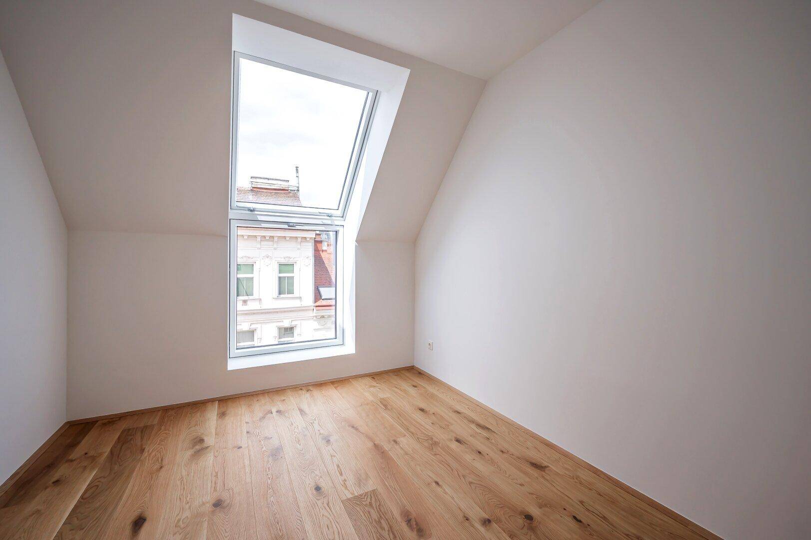 Helles Schlafzimmer im Dachgeschoss mit schrägen Wänden und großem Dachfenster für viel Licht.