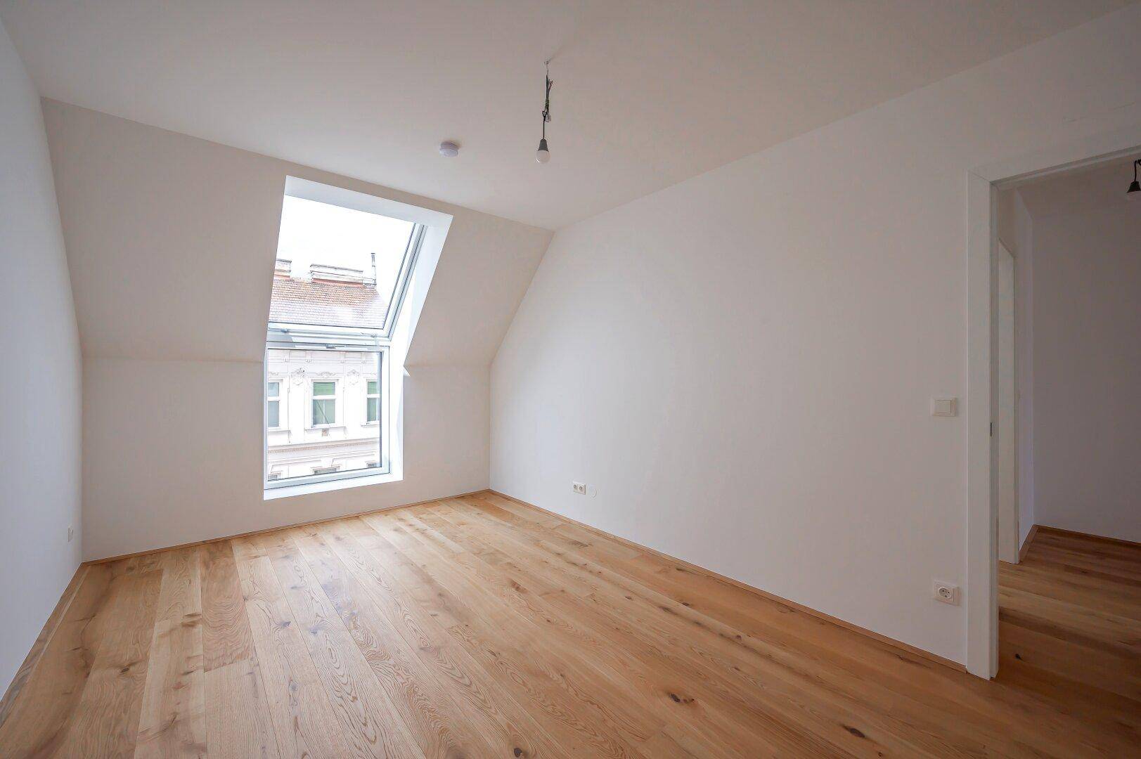 Gemütliches Schlafzimmer mit Holzboden und einem großen Dachfenster, das viel Tageslicht hereinlässt.