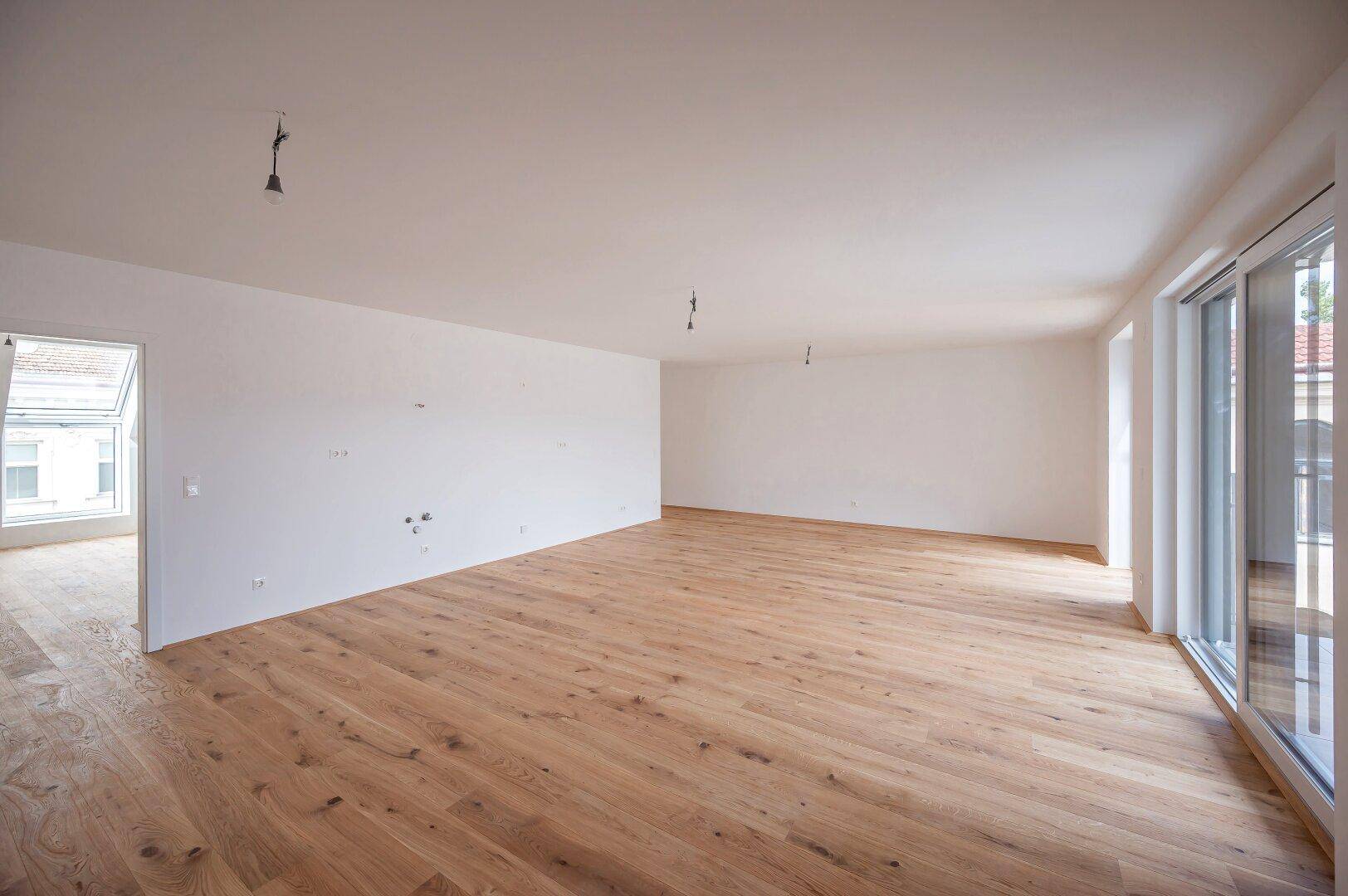 Großer, heller Wohnbereich mit Holzboden und viel Tageslicht durch die breite Fensterfront.
