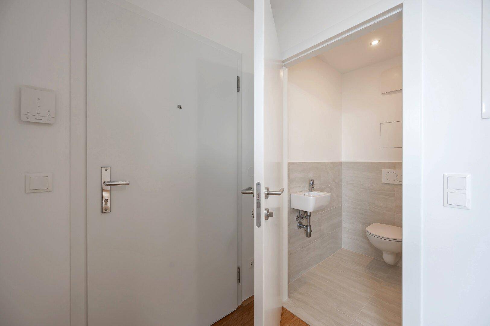 Modernes Gäste-WC mit Wand-WC, kleinem Waschbecken und hellen Fliesen, in neuwertigem Zustand.