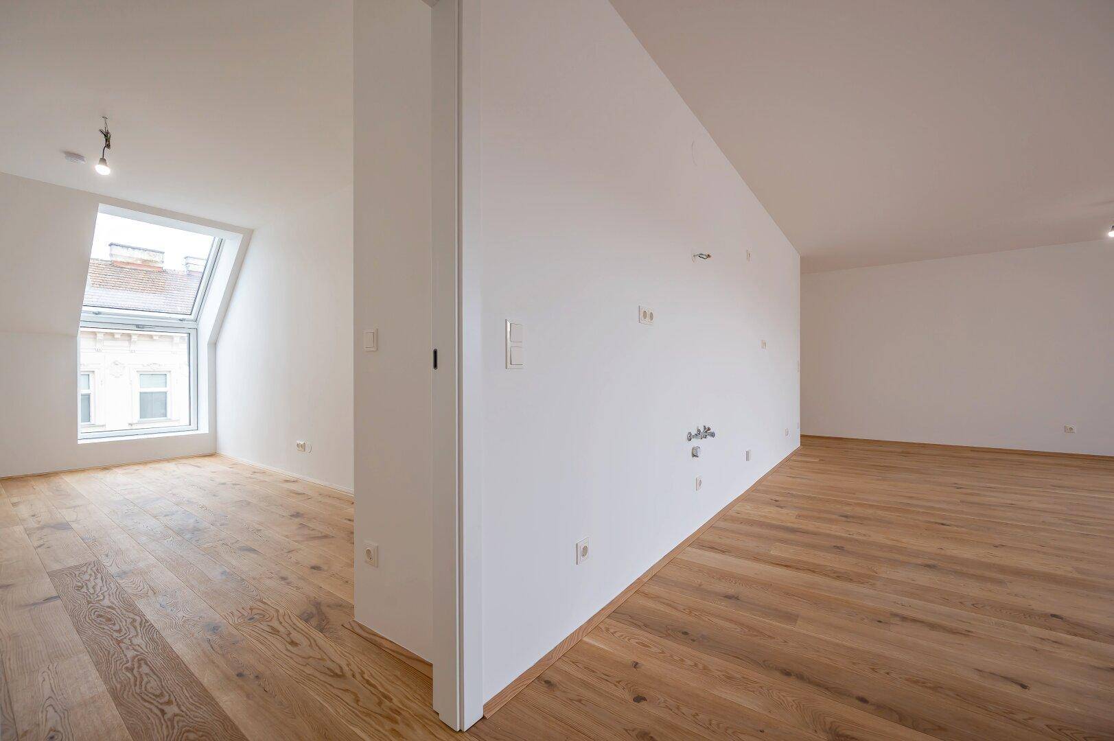 Offener Bereich mit Holzboden und einer Trennwand, die verschiedene Zonen im Raum schafft.