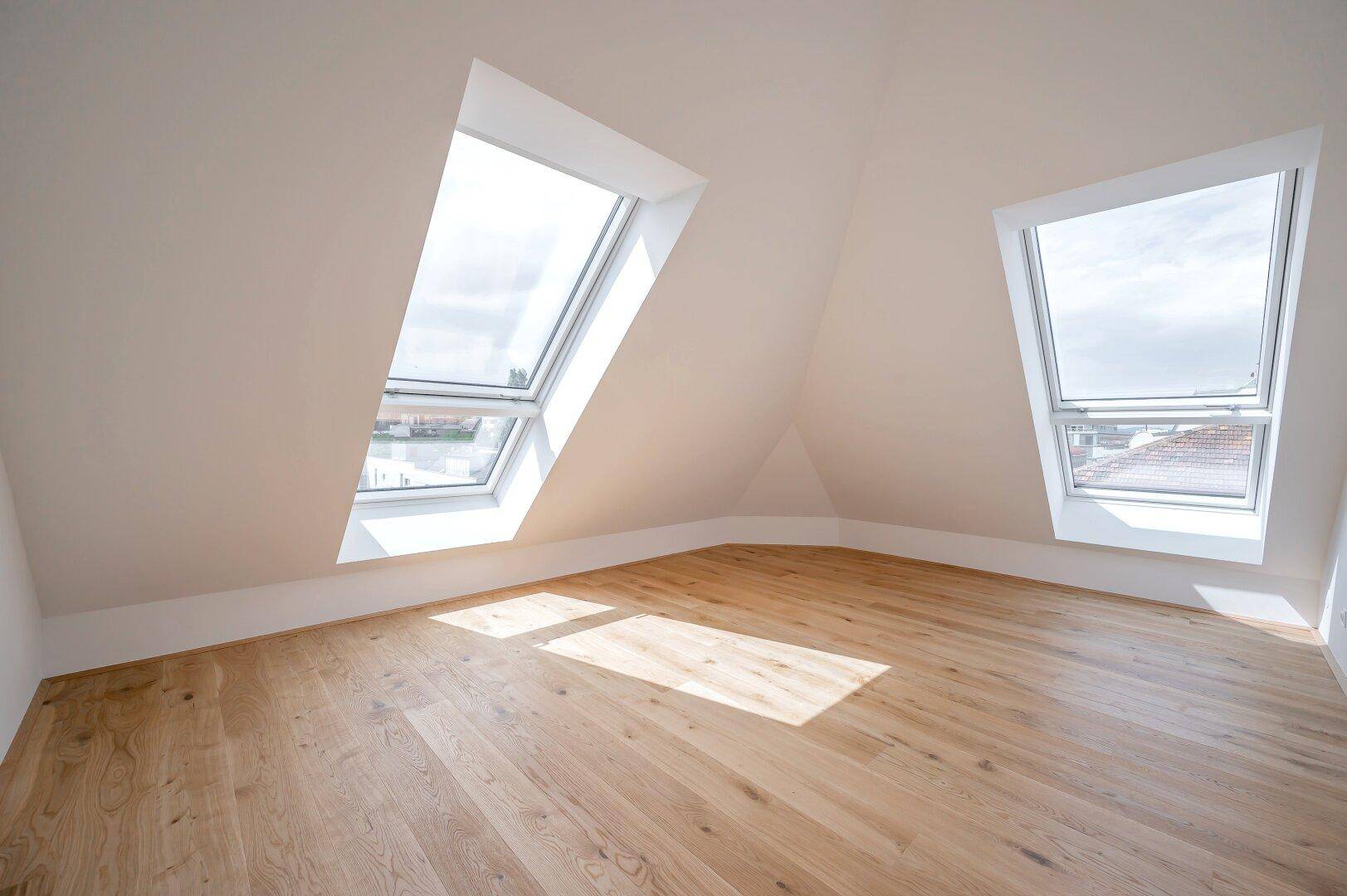 Geräumiges Dachgeschosszimmer mit zwei großen Dachfenstern und hellem Holzfußboden.